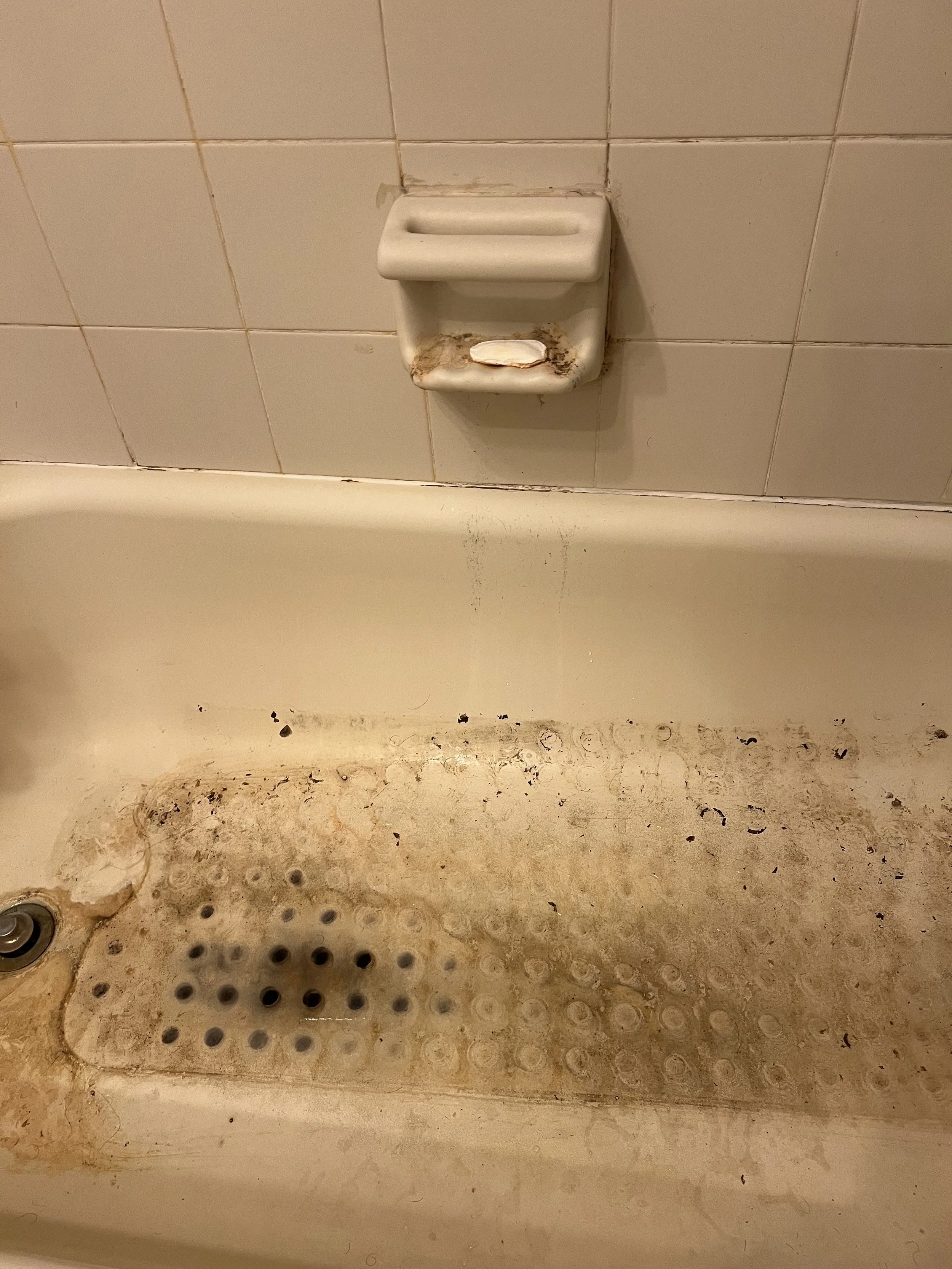 Dirty bathtub with mold and grime, soap dish with soap, surrounded by stained tiles.