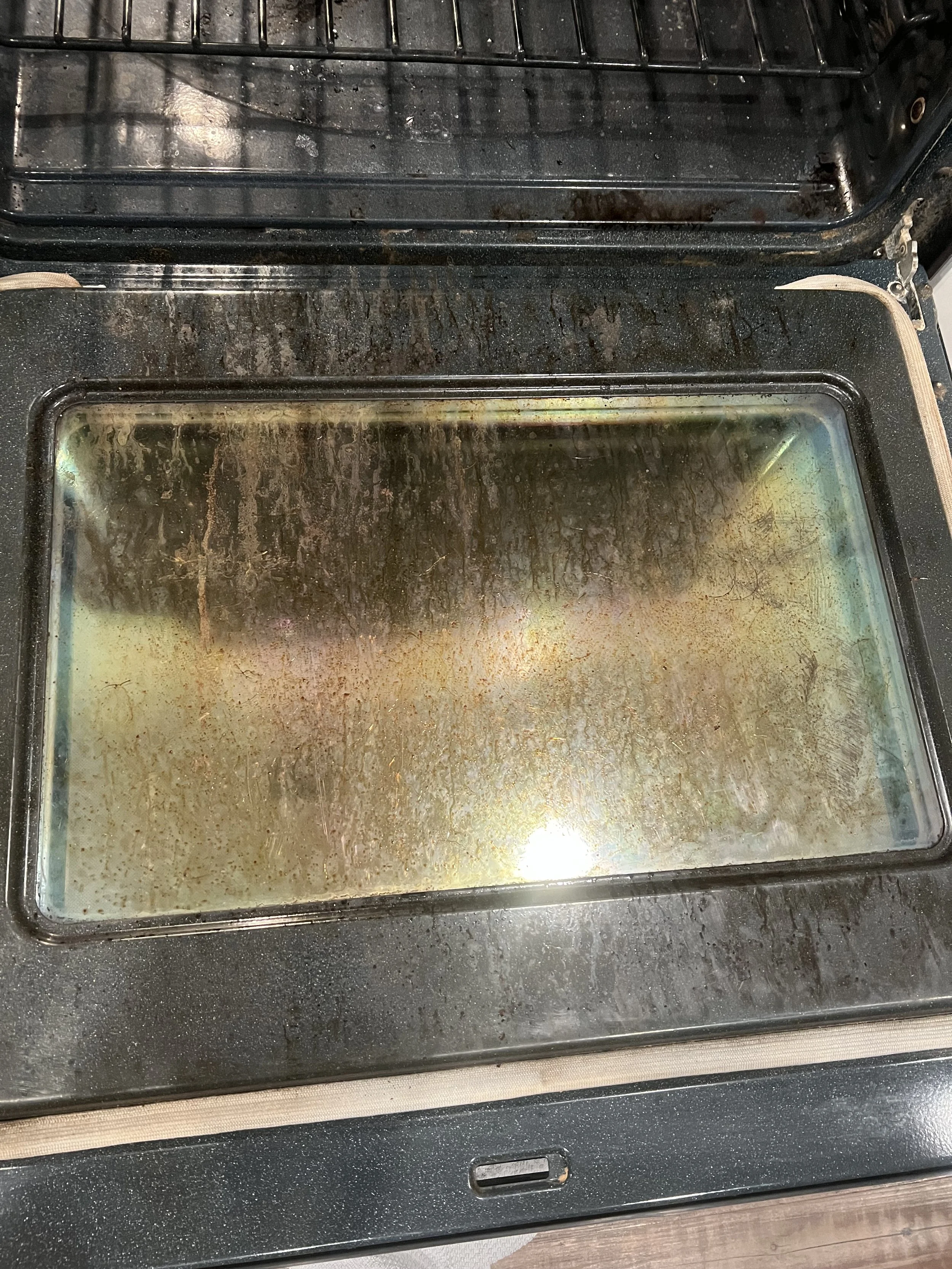 Oven with a dirty glass door that has accumulated smoke and grease stains.
