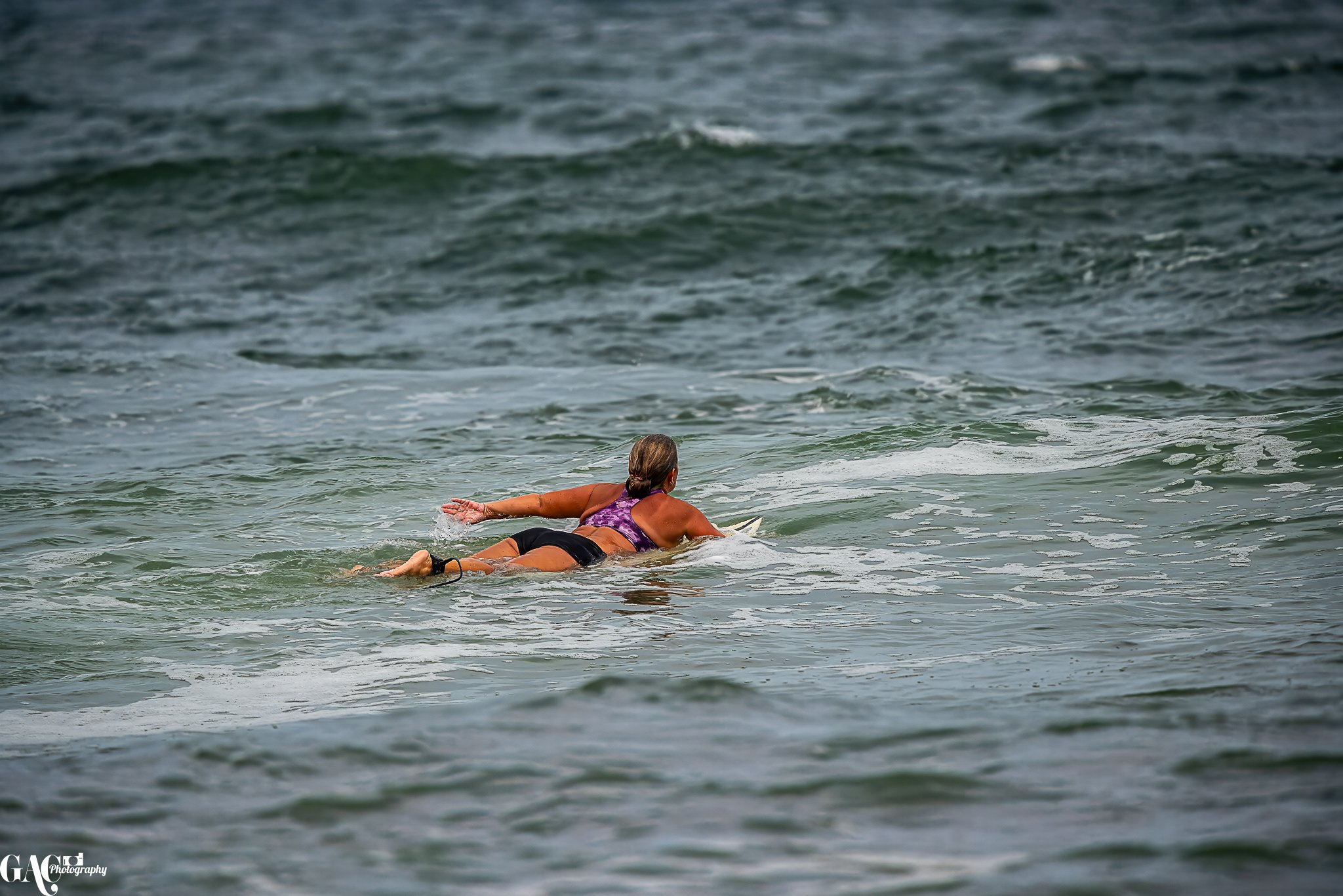 A woman lying on a surfboard paddling in the ocean waves.