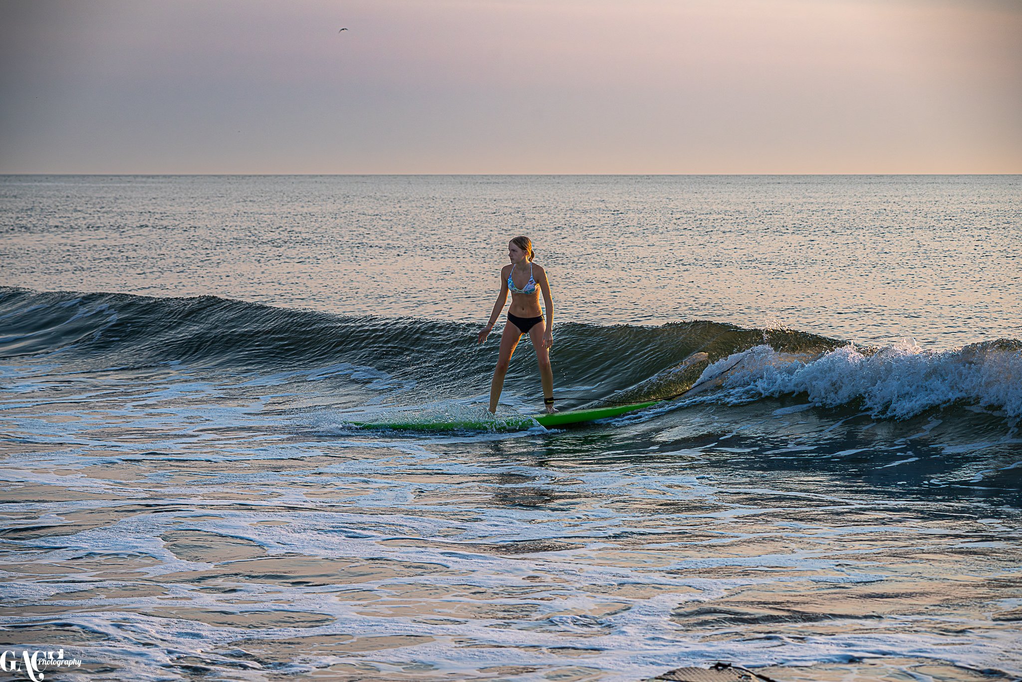 A woman surfing on a green surfboard in the ocean at sunset.