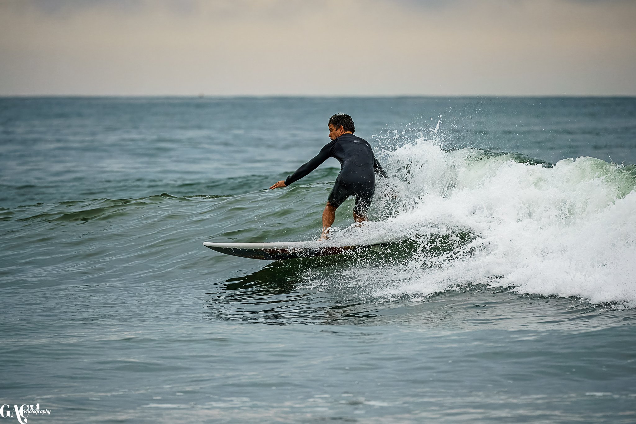 Man surfing on the ocean wearing a black wetsuit during daytime.