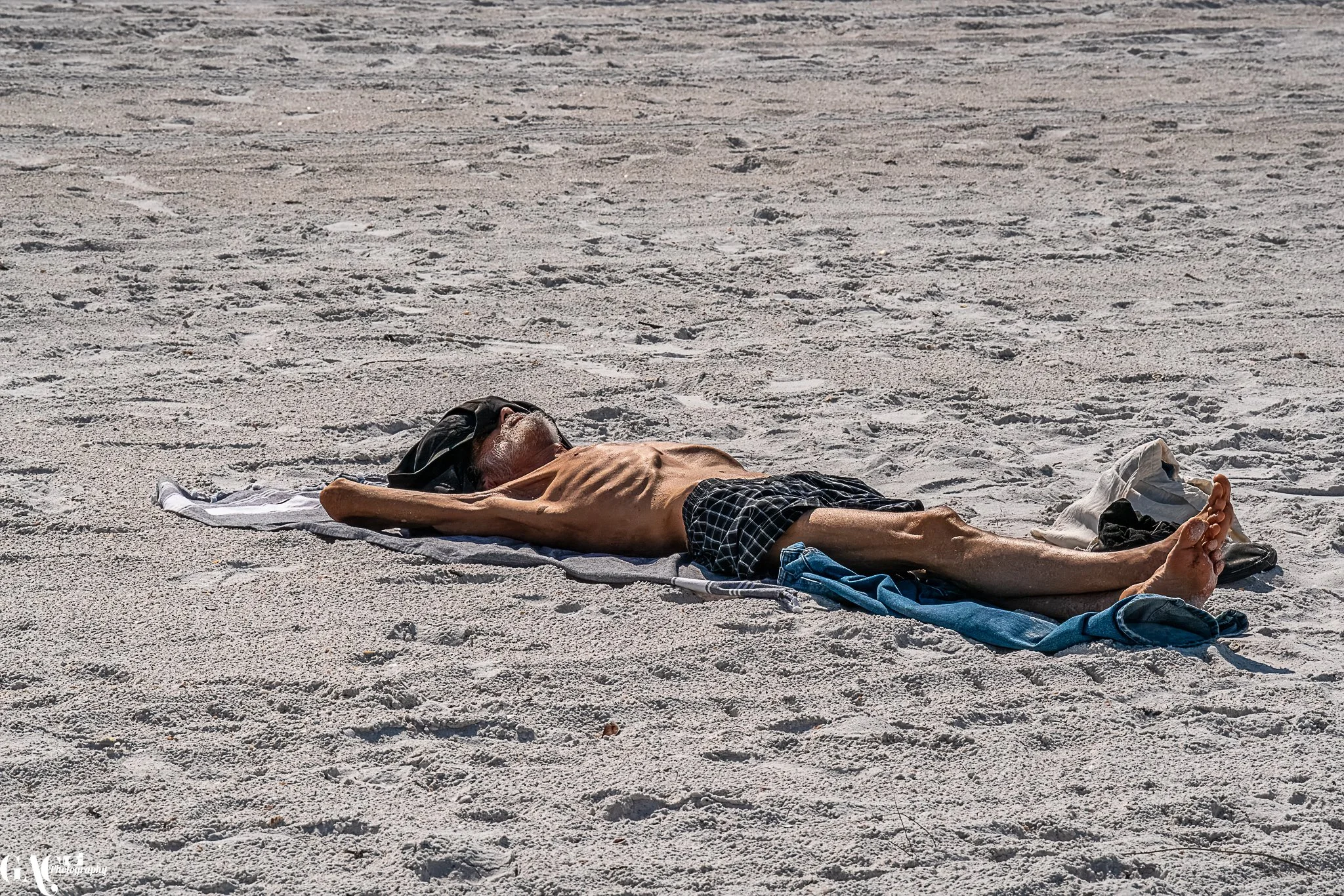 Person sunbathing on a sandy beach, lying on a towel with arms stretched out.