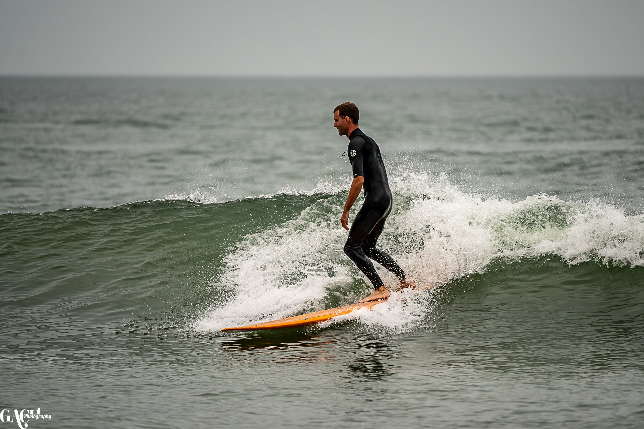 A man surfing on a small wave in the ocean during cloudy weather.