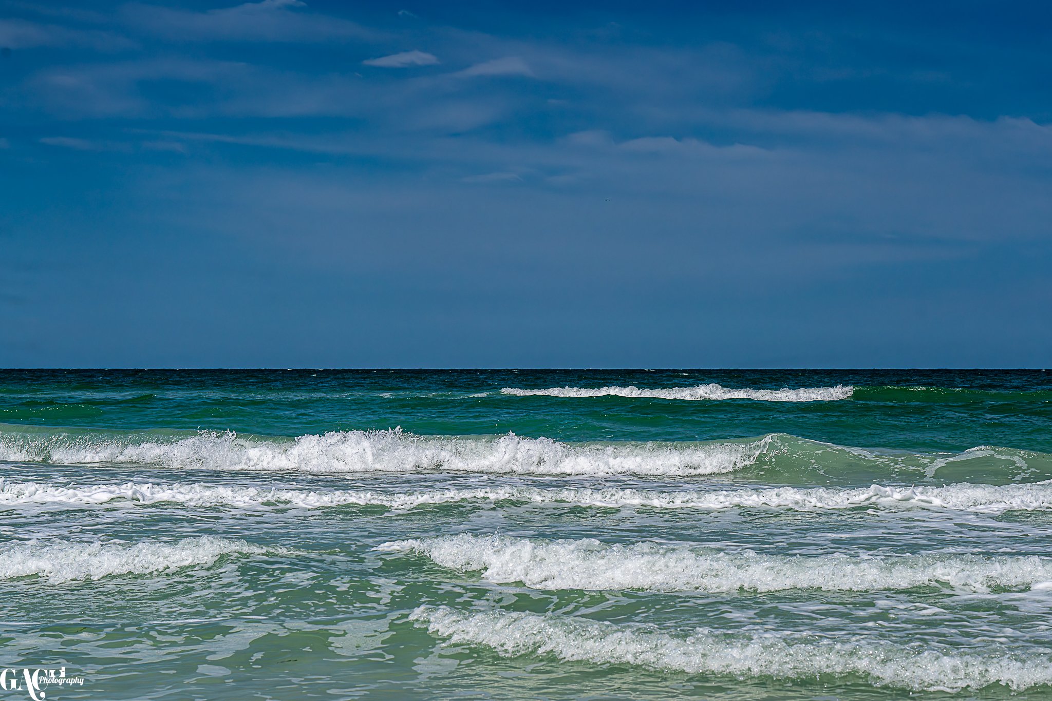 Ocean waves crashing onto the sandy beach under a partly cloudy sky.