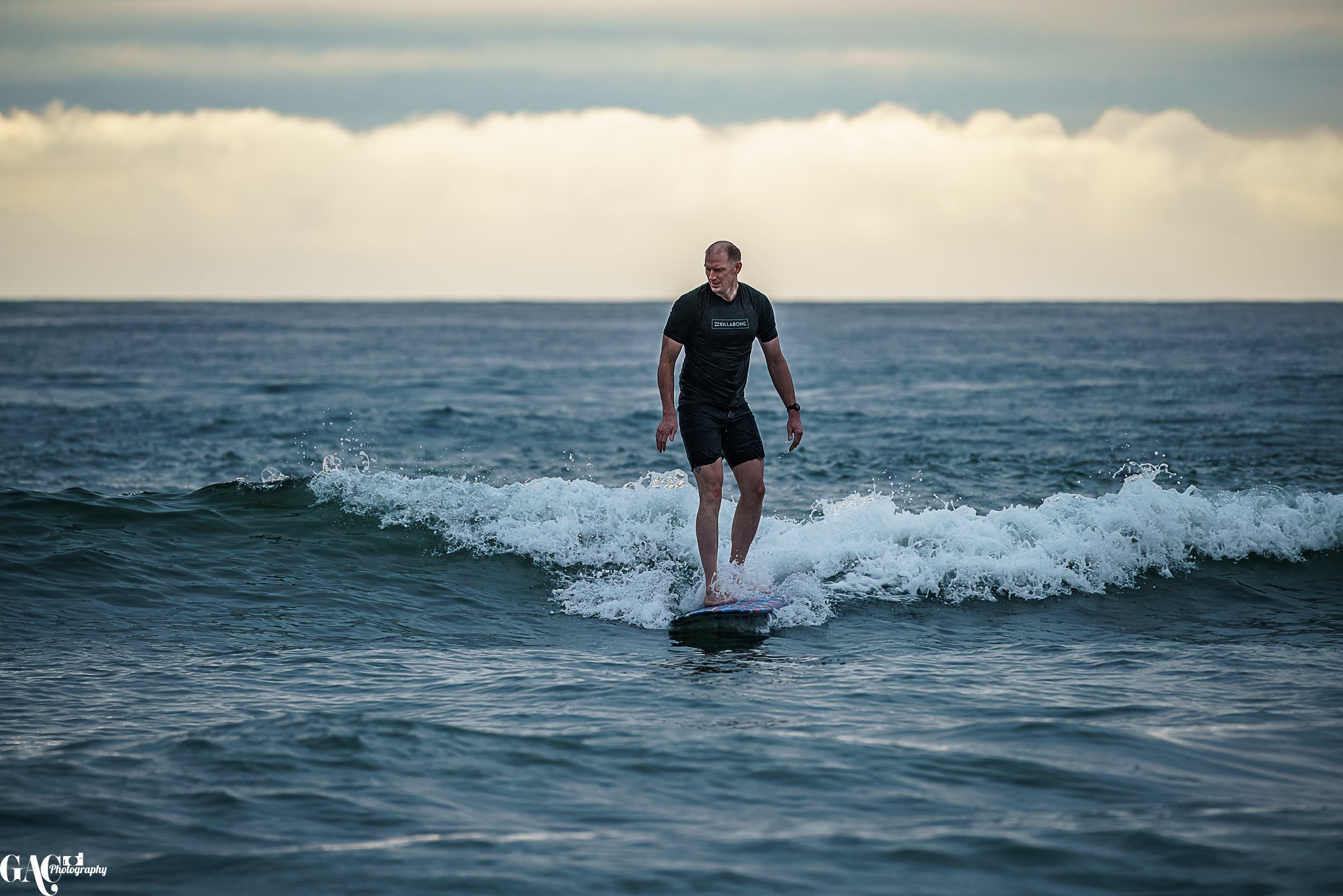 A man surfboarding on the ocean waves during sunset or sunrise.