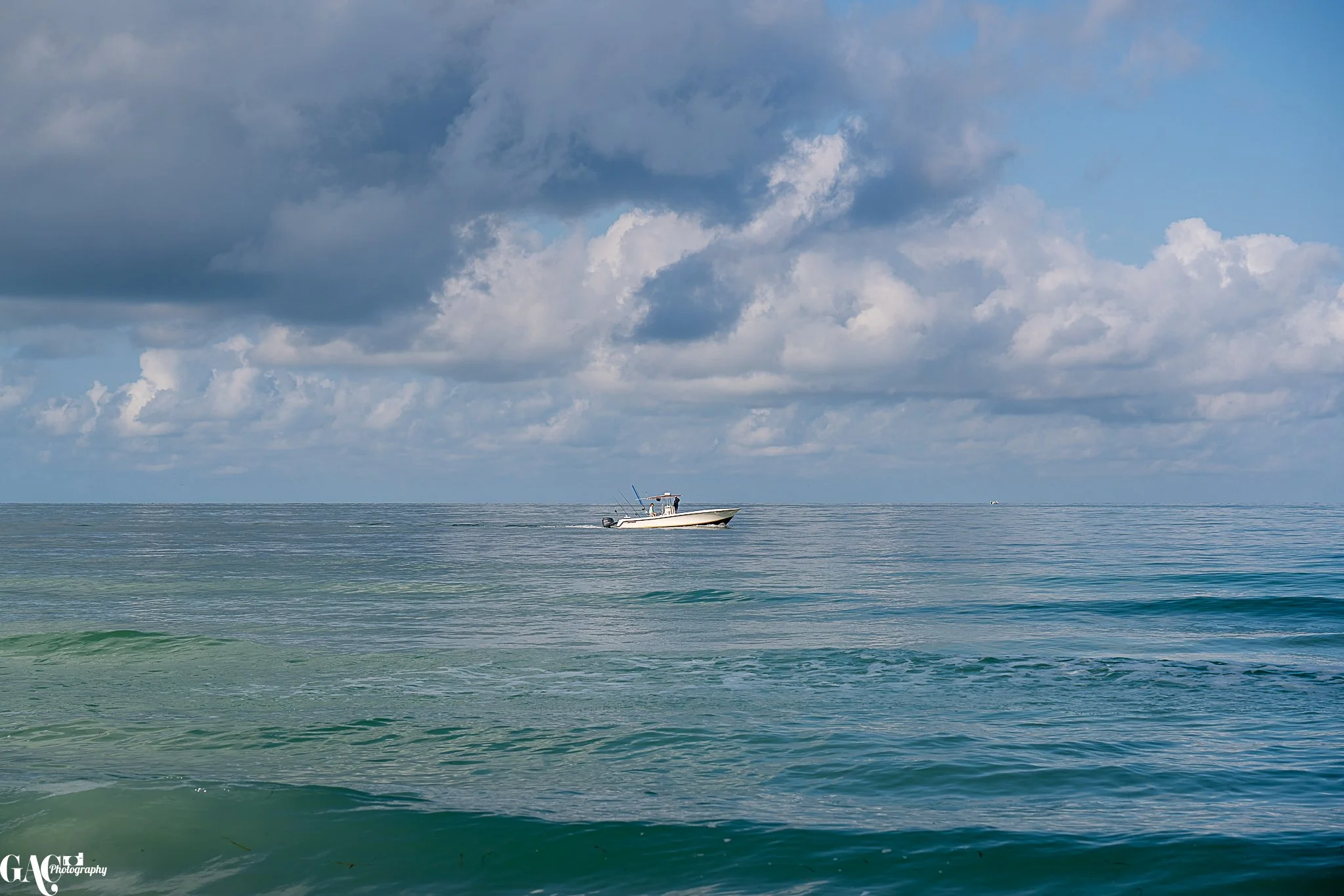 A boat sailing on calm ocean water under cloudy sky.