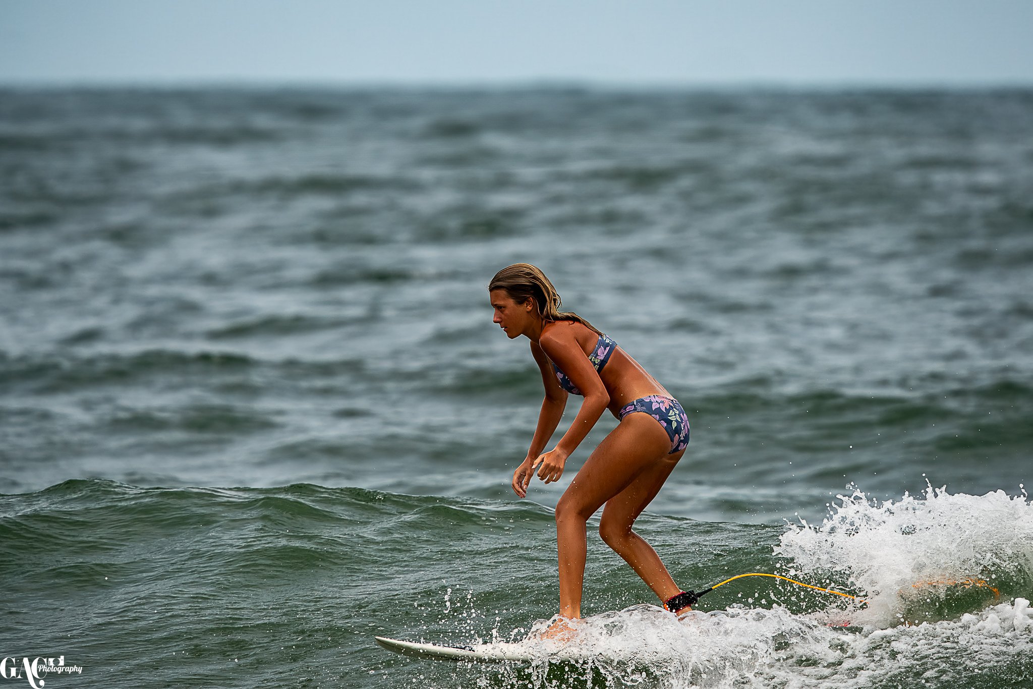 A woman in a floral bikini surfing on a small wave in the ocean.
