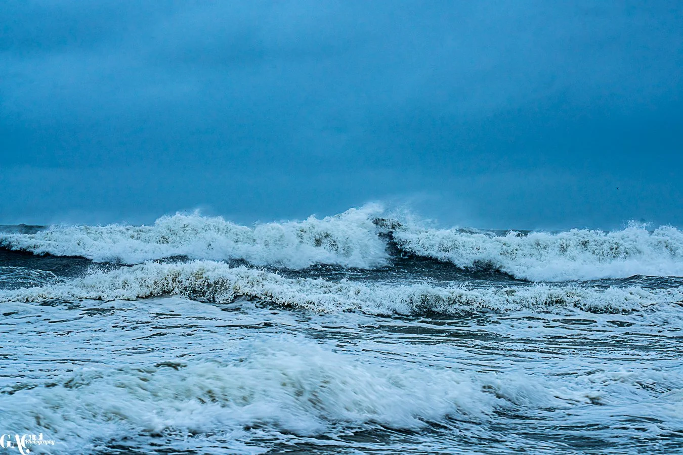 Ocean waves crashing under a cloudy sky.
