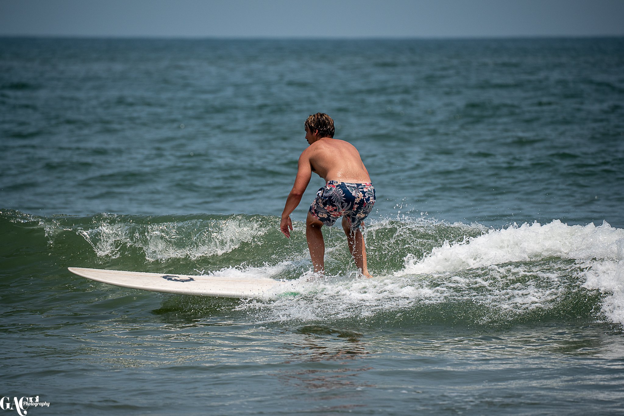 Man surfing on a wave in the ocean, wearing floral swim shorts.