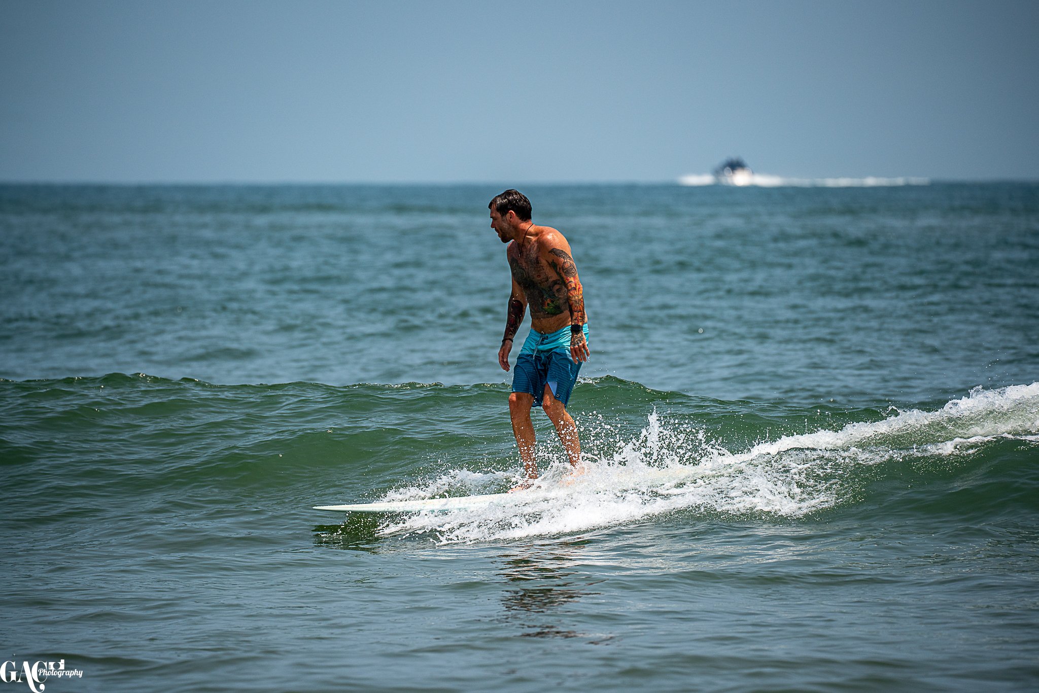 A man with tattoos wearing blue shorts surfing on a small wave in the ocean.