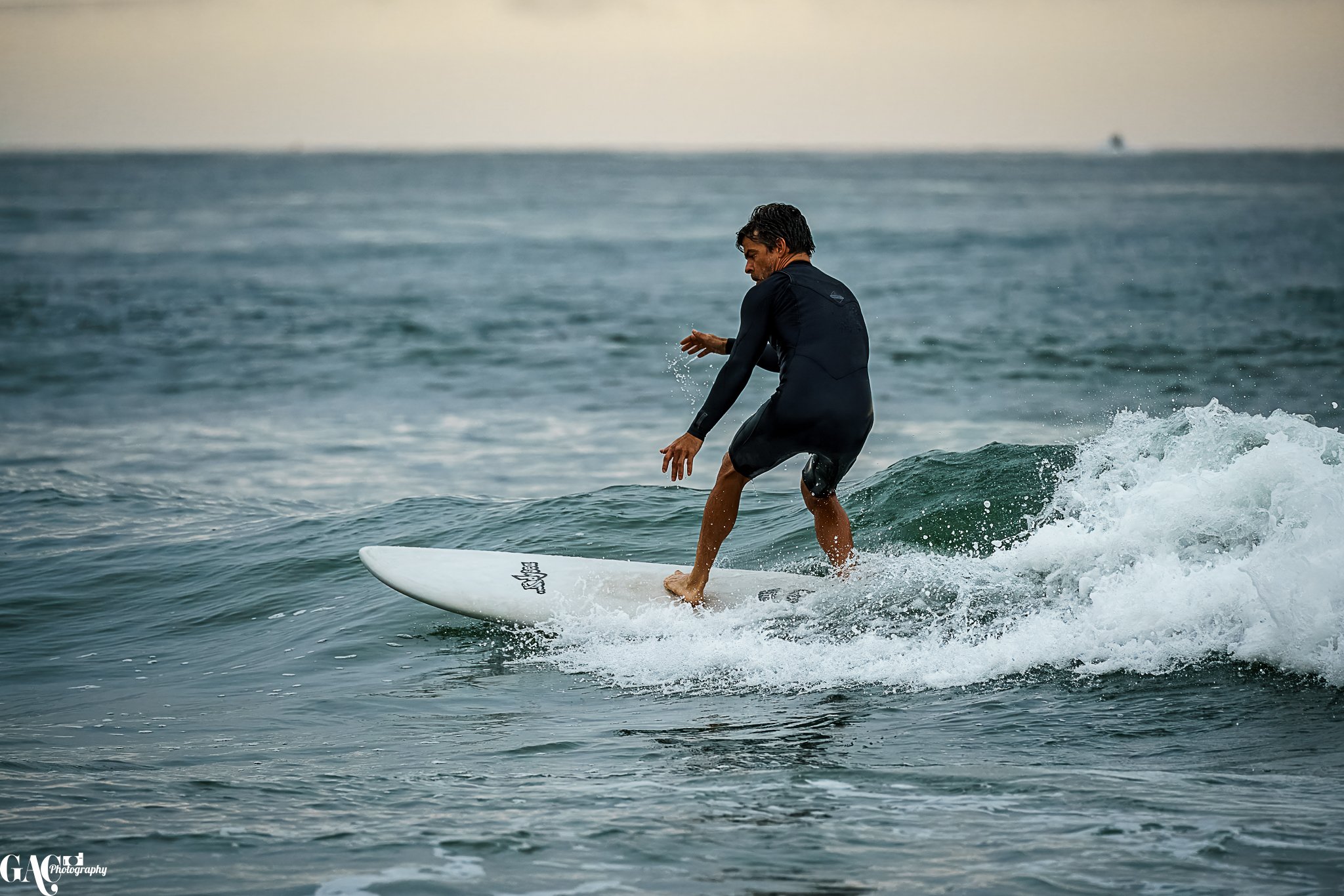 Man surfing on a wave in the ocean during sunset or sunrise.