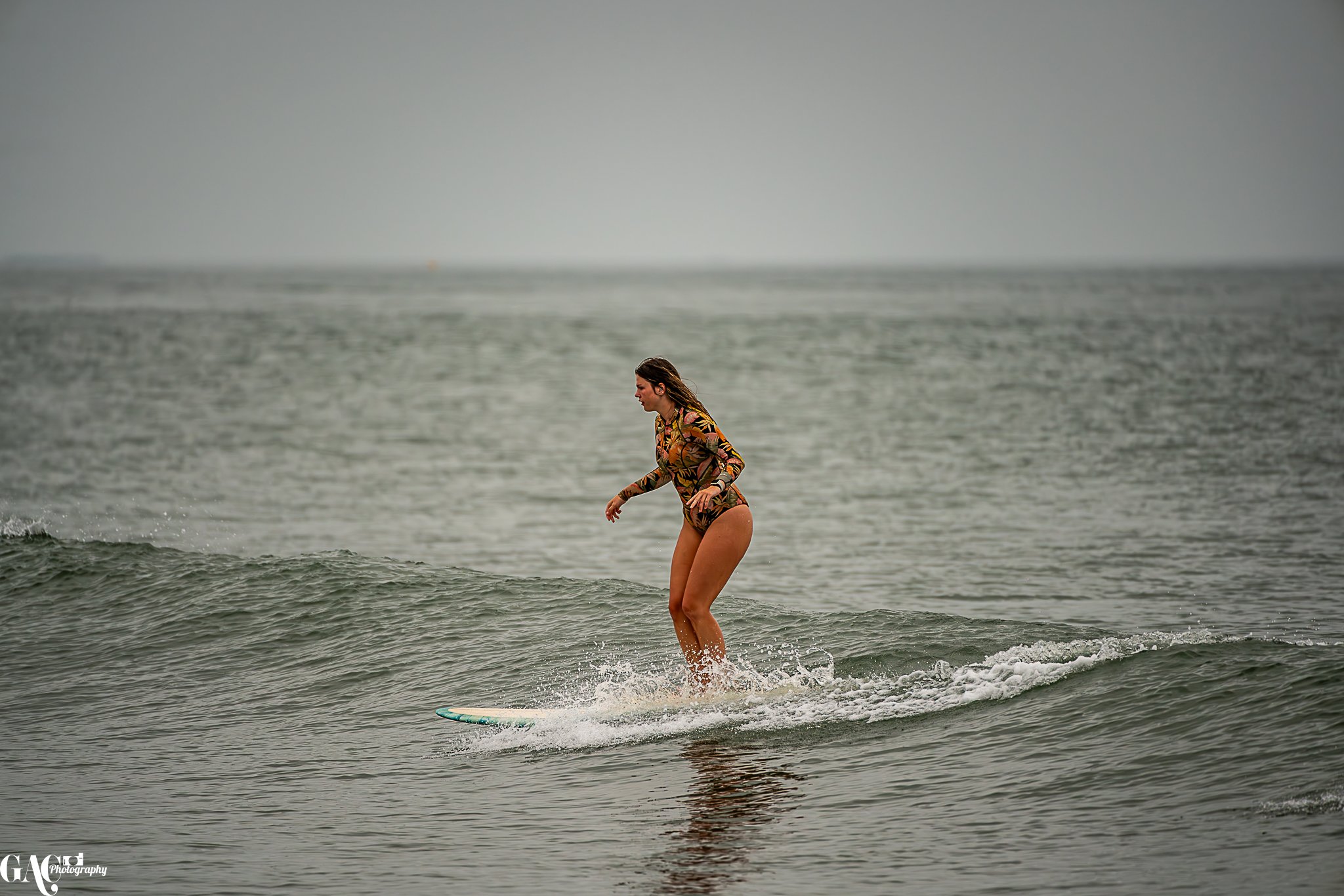A woman surfing on a small wave in the ocean, wearing a long-sleeve rash guard with a floral pattern.