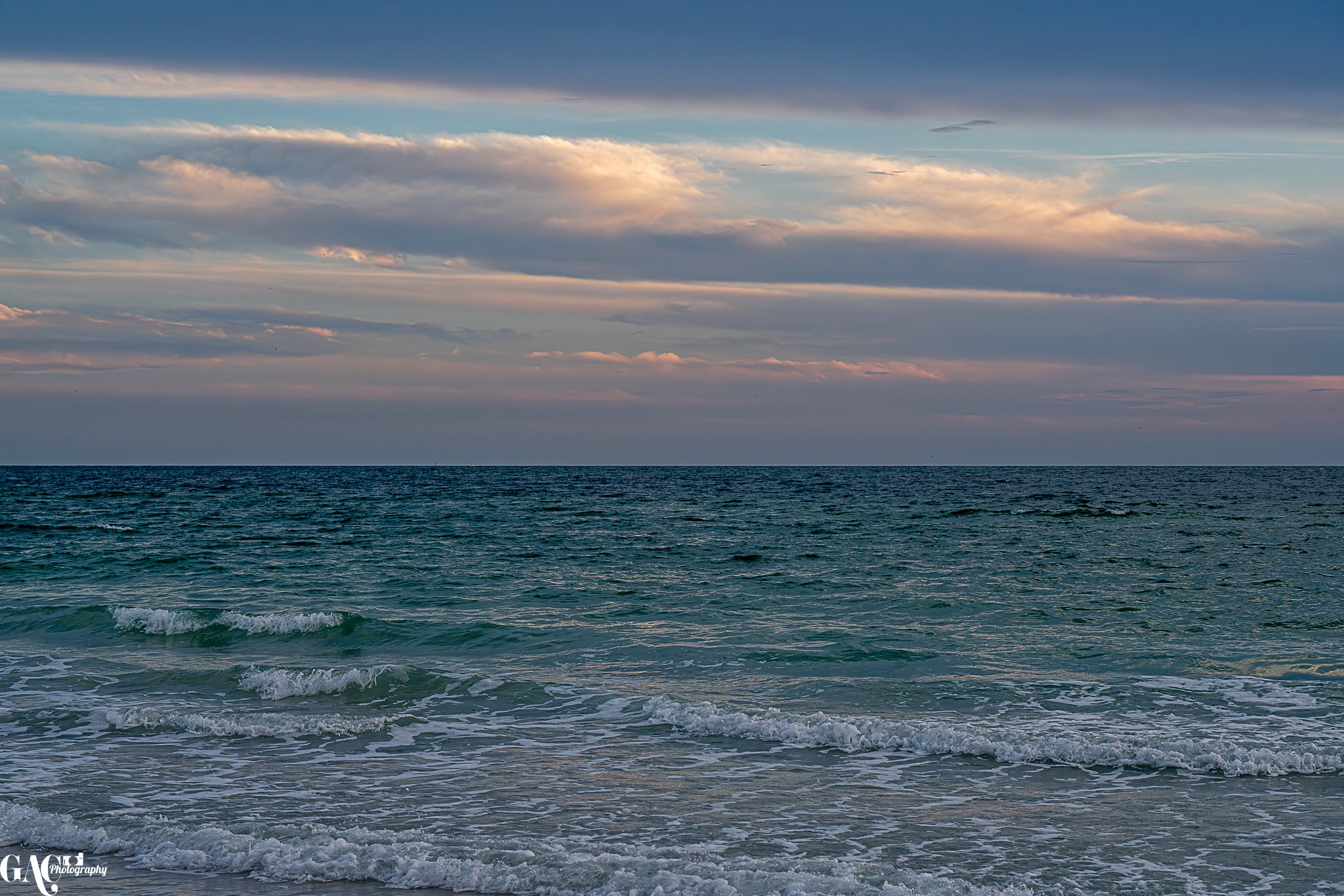 A calm ocean with gentle waves under a partly cloudy sky during sunset or sunrise.