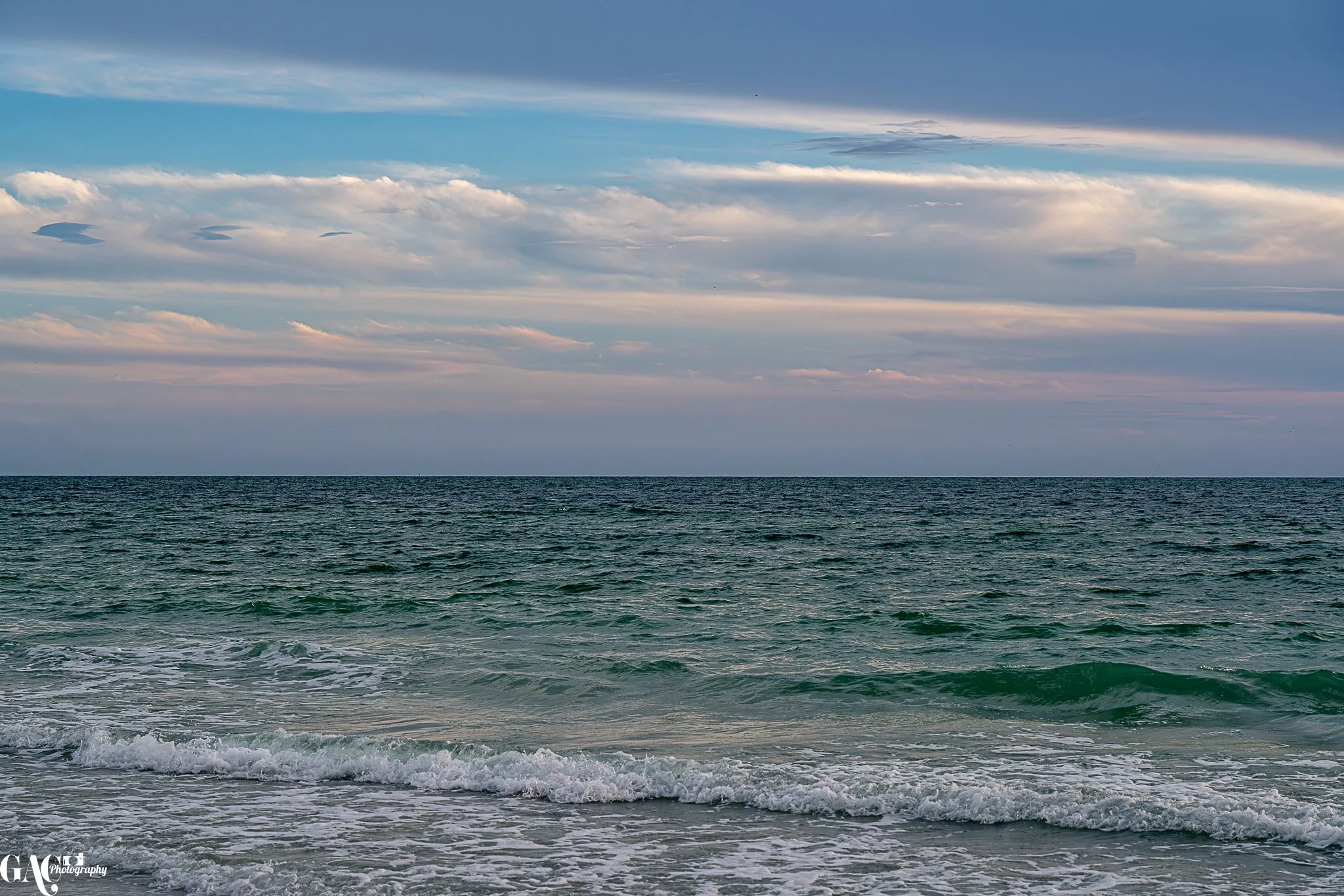 Calm ocean waves with a clear blue sky and scattered clouds.