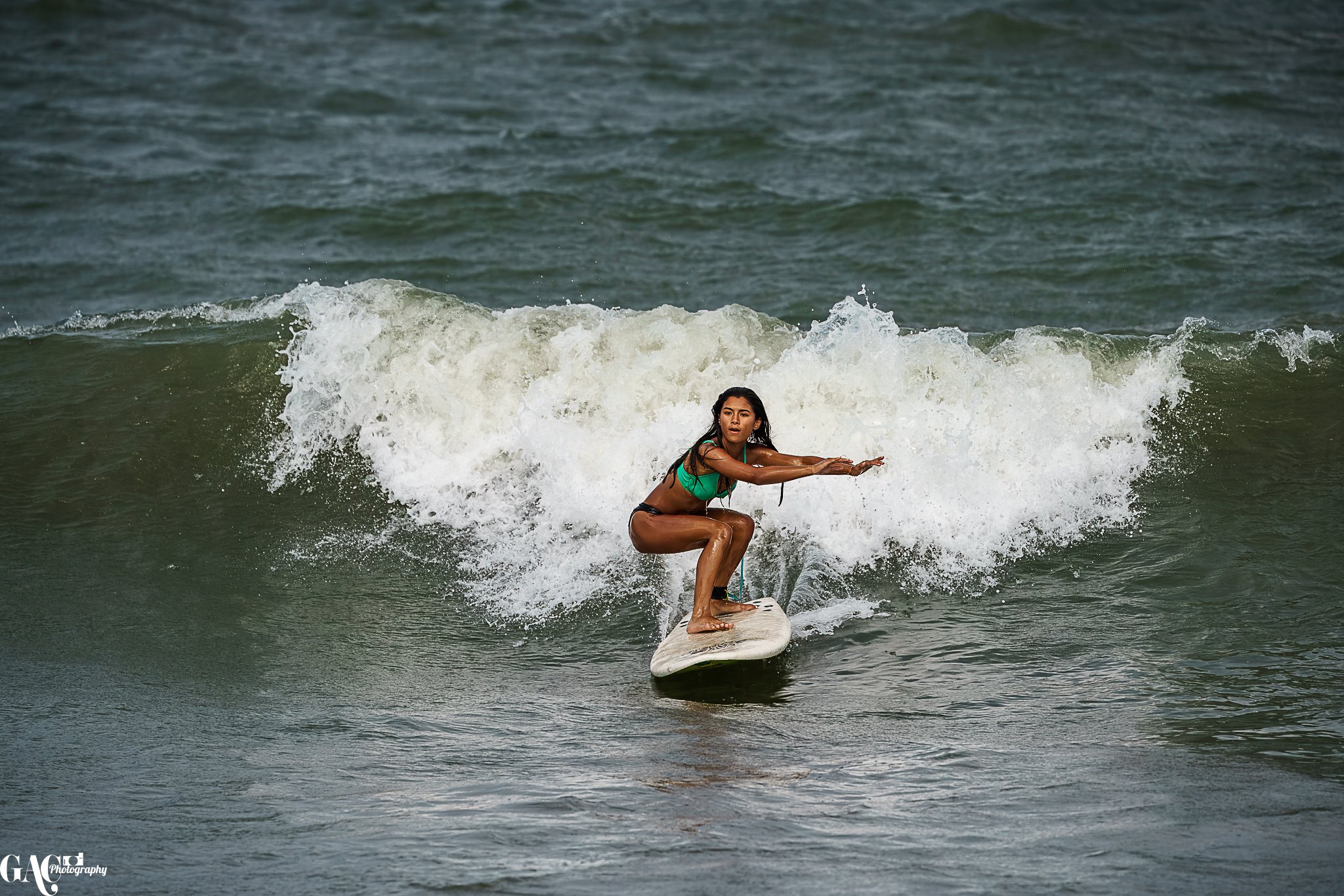 A woman surfing on a wave in the ocean, wearing a green top and black shorts.