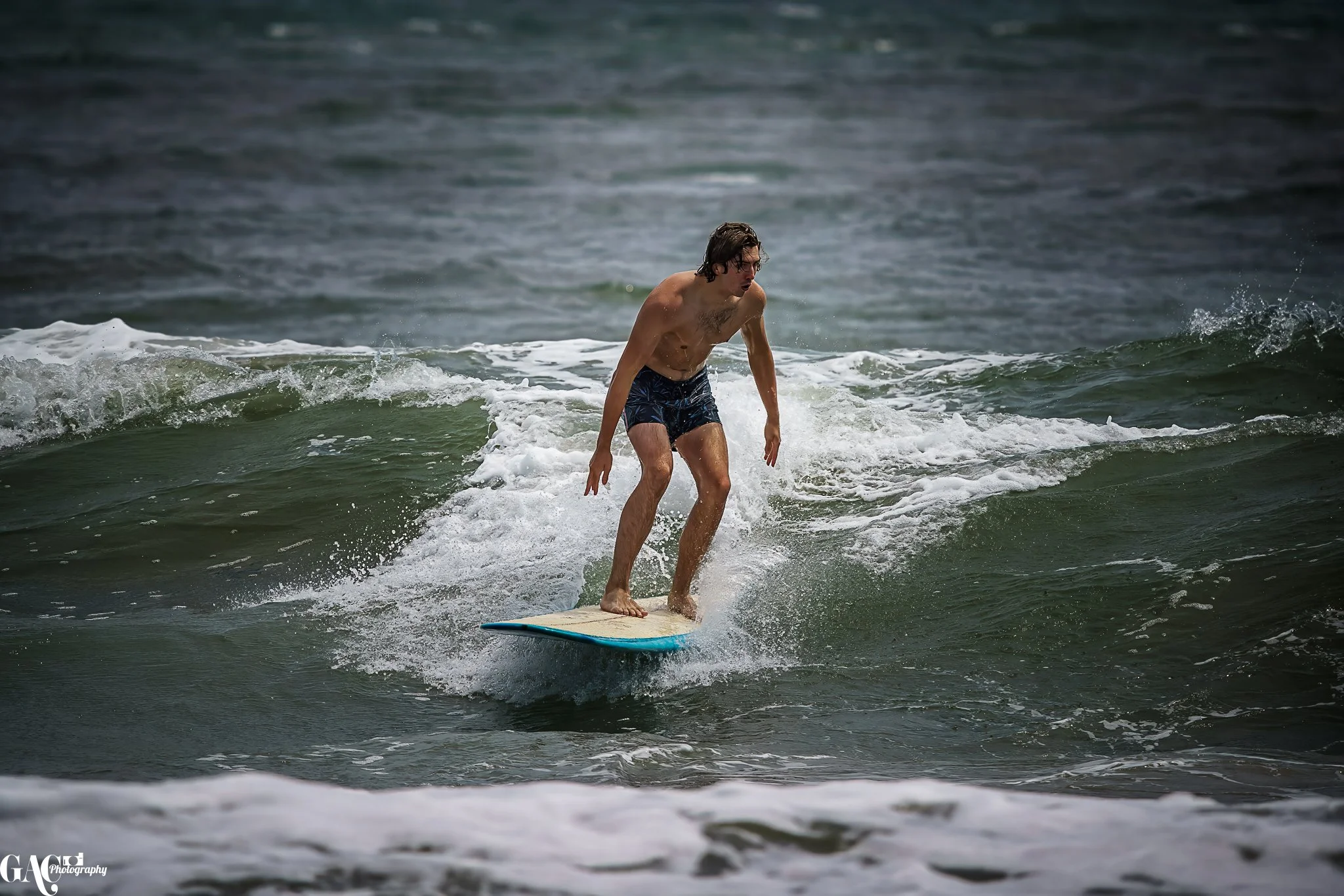 A man surfing on a wave in the ocean, wearing blue swim shorts and no shirt.