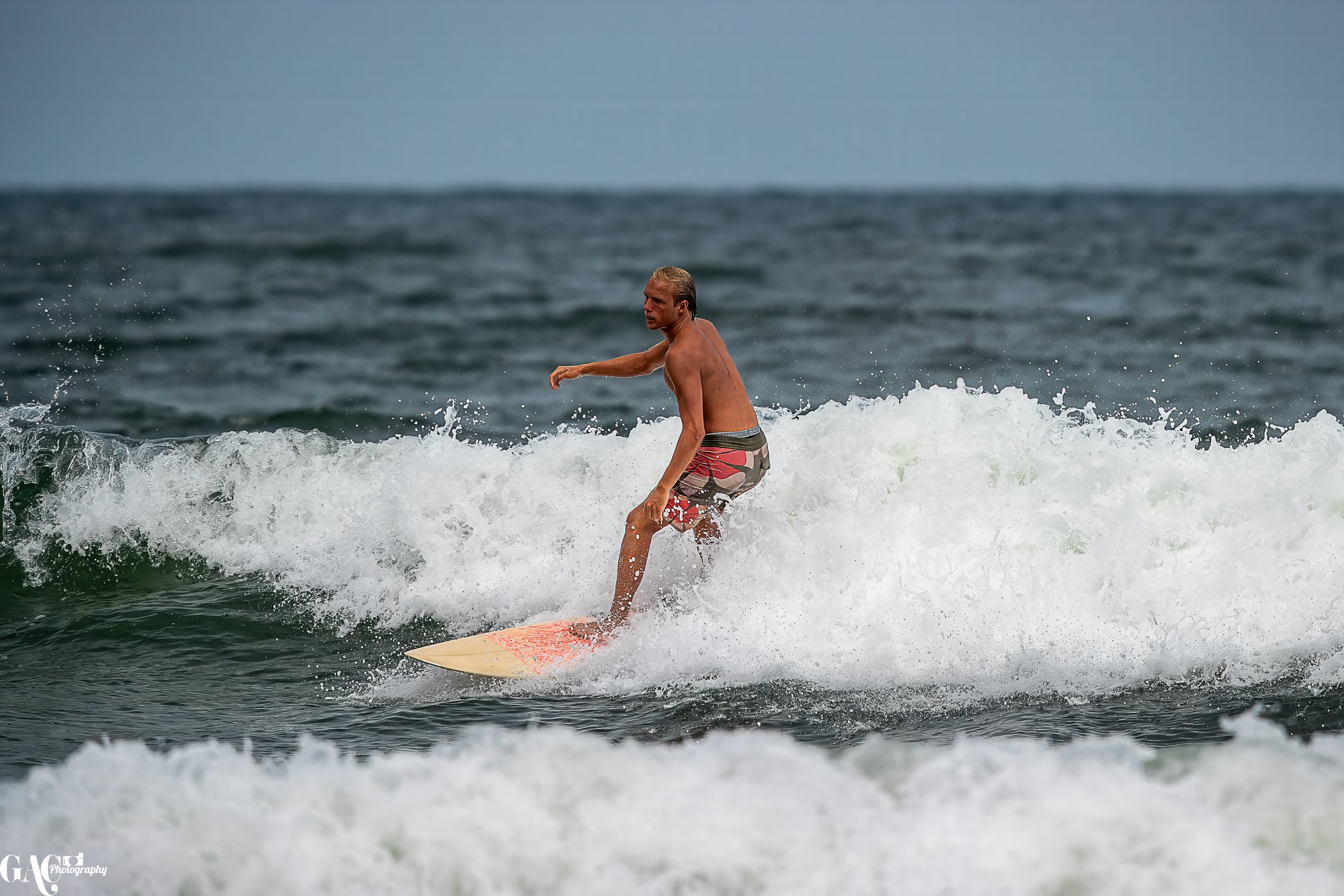 A man surfing on a wave in the ocean, wearing swim trunks, with water splashing around him.