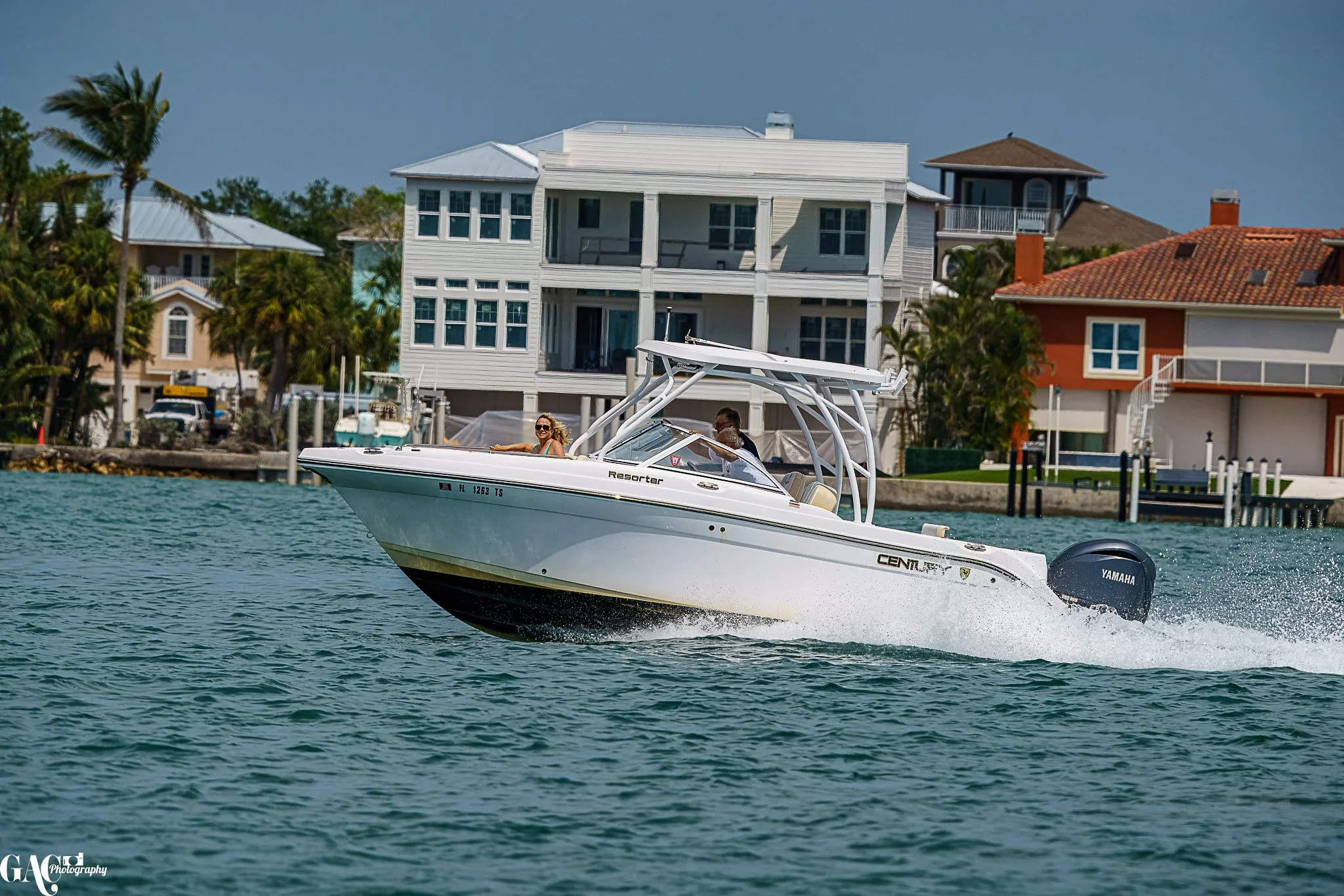 Motorboat cruising on a waterway with waterfront houses and palm trees in the background.