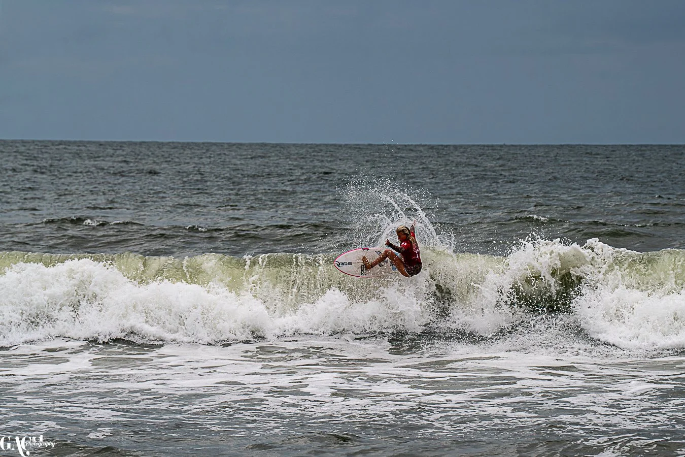 A person surfing on a wave in the ocean during overcast weather.