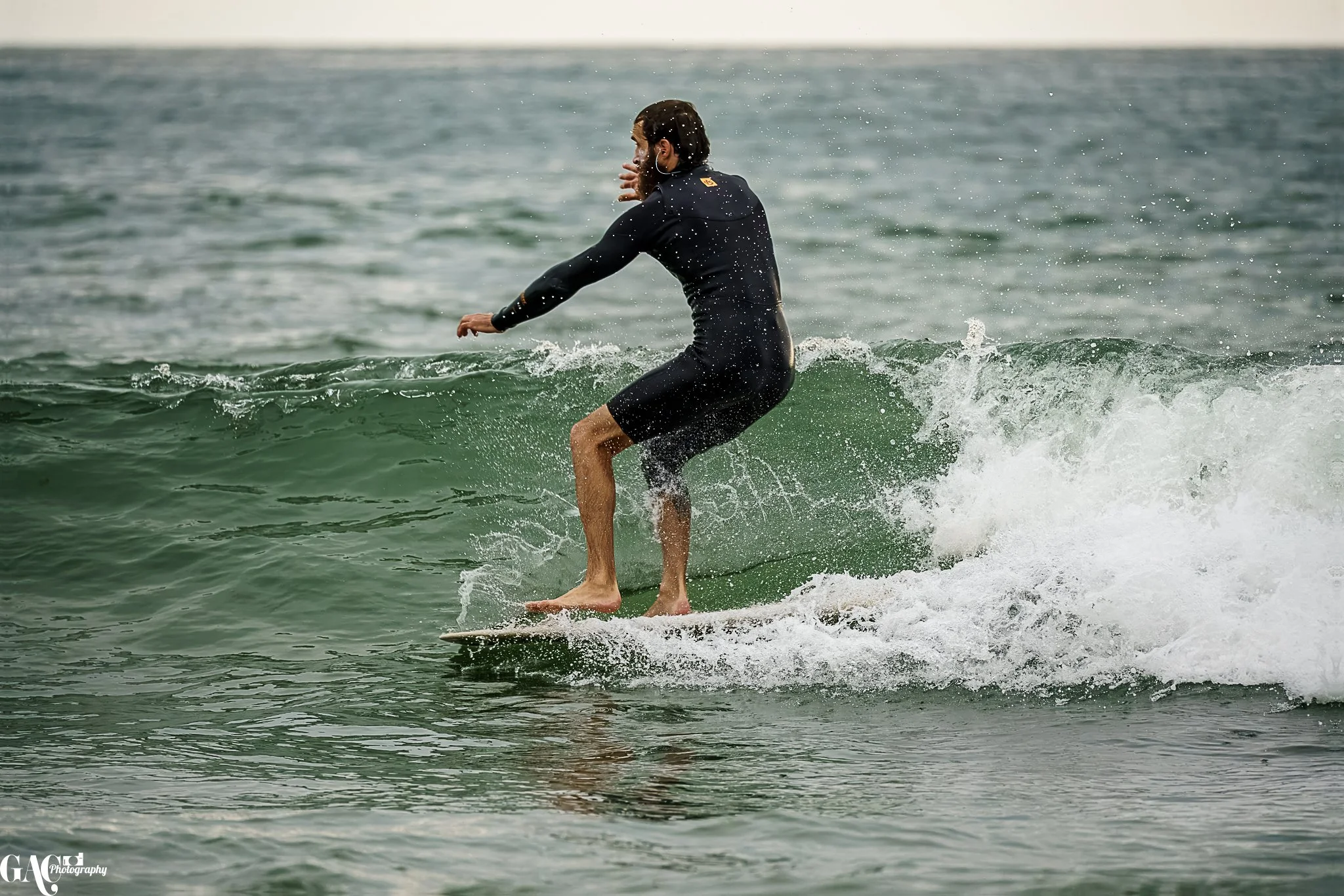 A man surfing on a small wave in the ocean, wearing a black wetsuit.