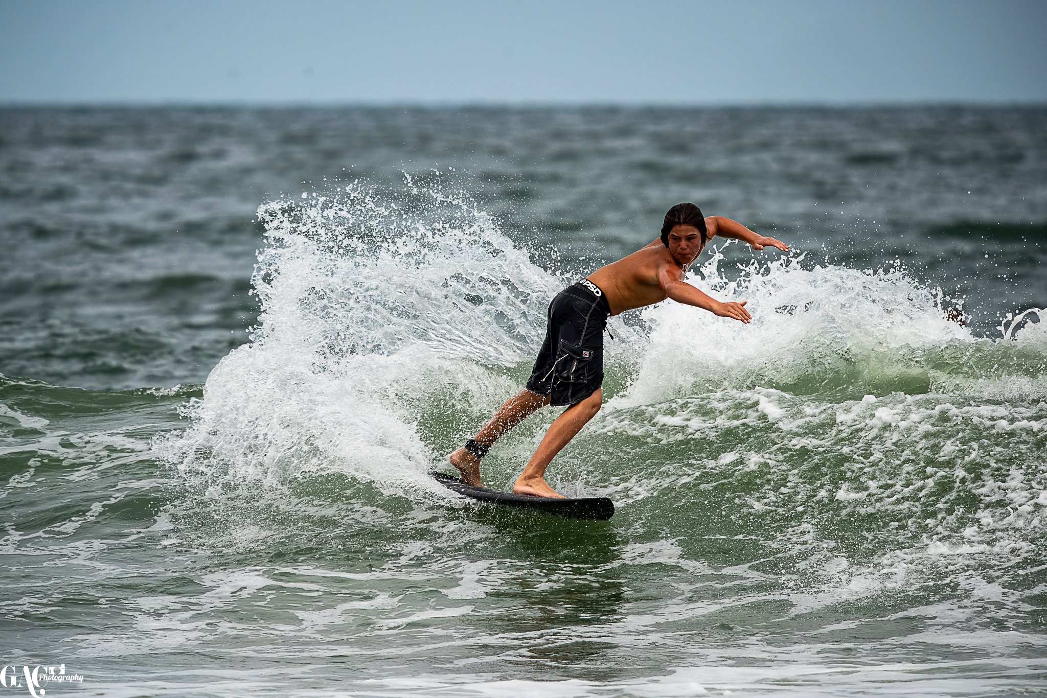 A man surfing on a wave in the ocean, wearing black shorts.