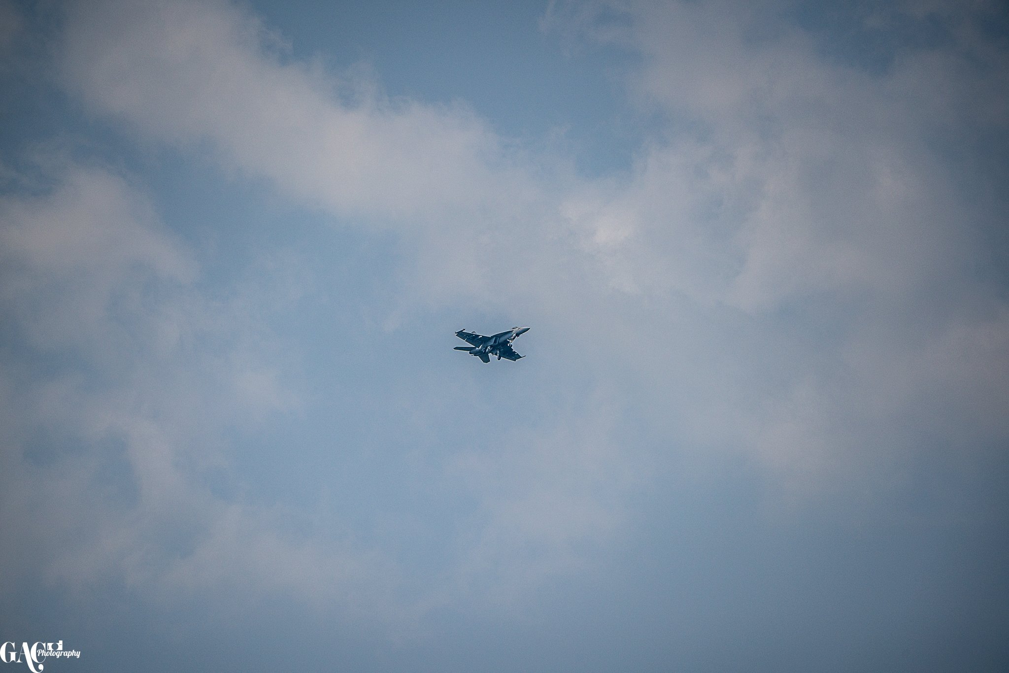 A military fighter jet flying through a partly cloudy sky.