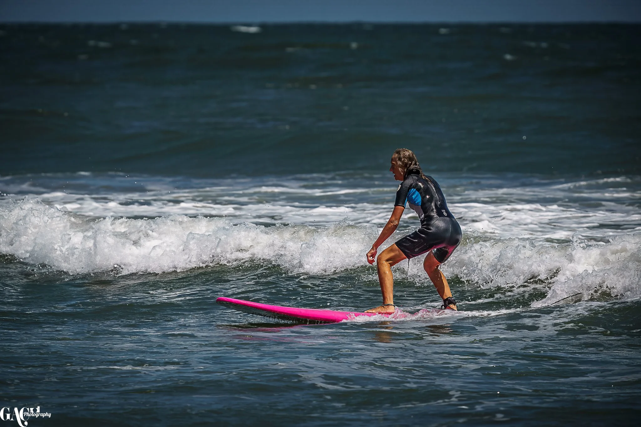 A person surfing on a pink surfboard in the ocean, wearing a wetsuit and balancing on a small wave.