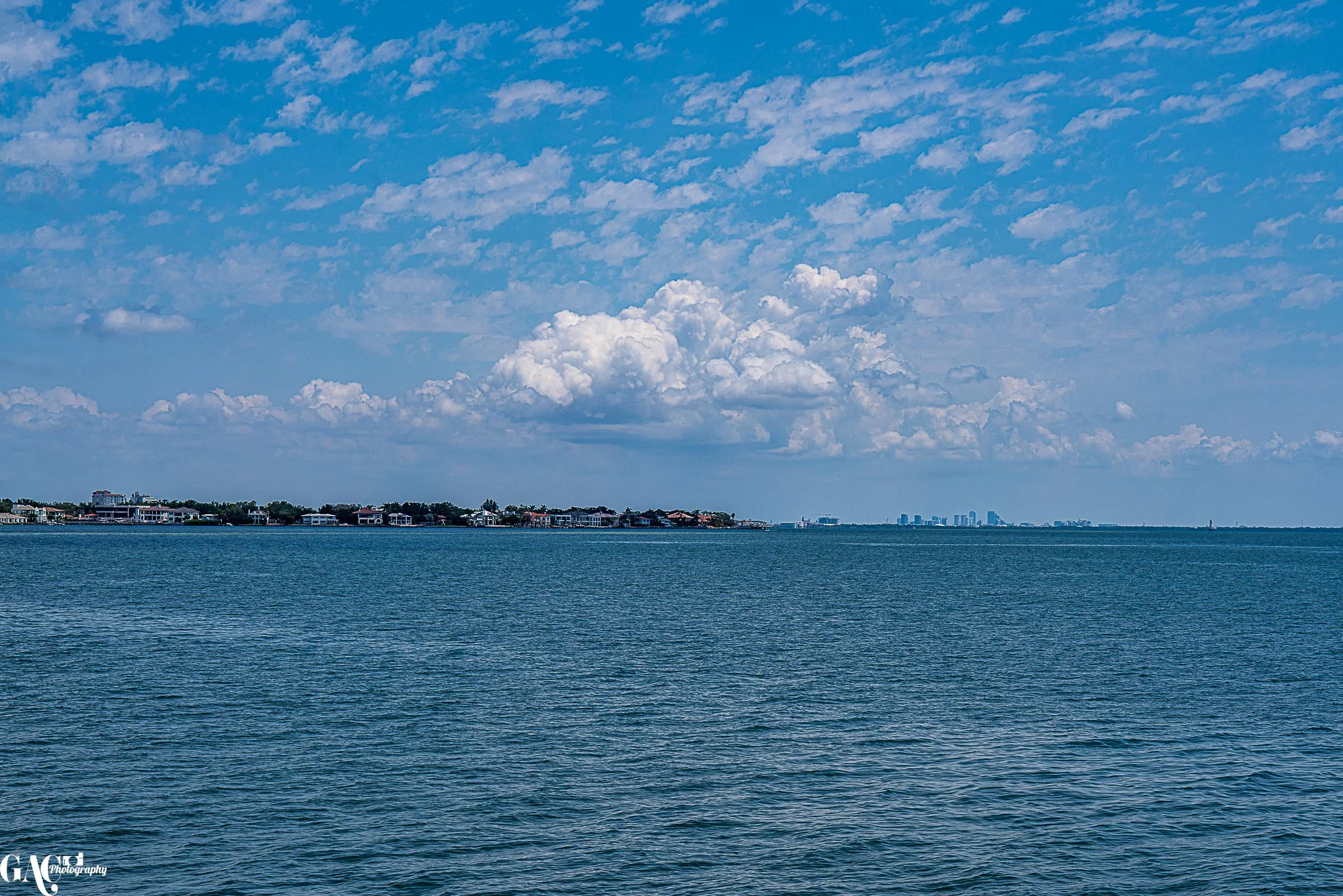 Ocean view with a distant shoreline, buildings, and a cloudy sky.