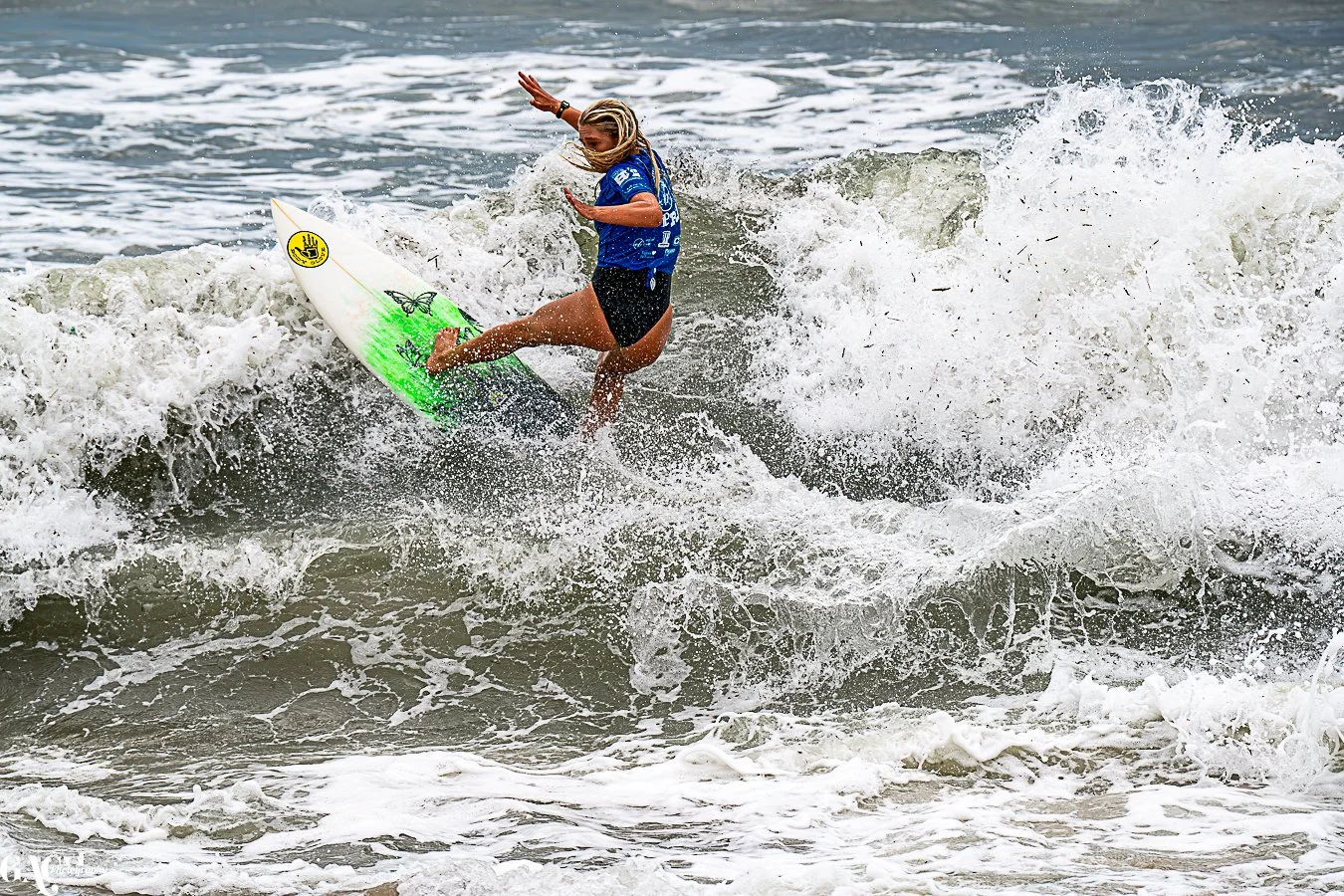 A woman with blonde hair surfing on a wave with a green and white surfboard in the ocean.