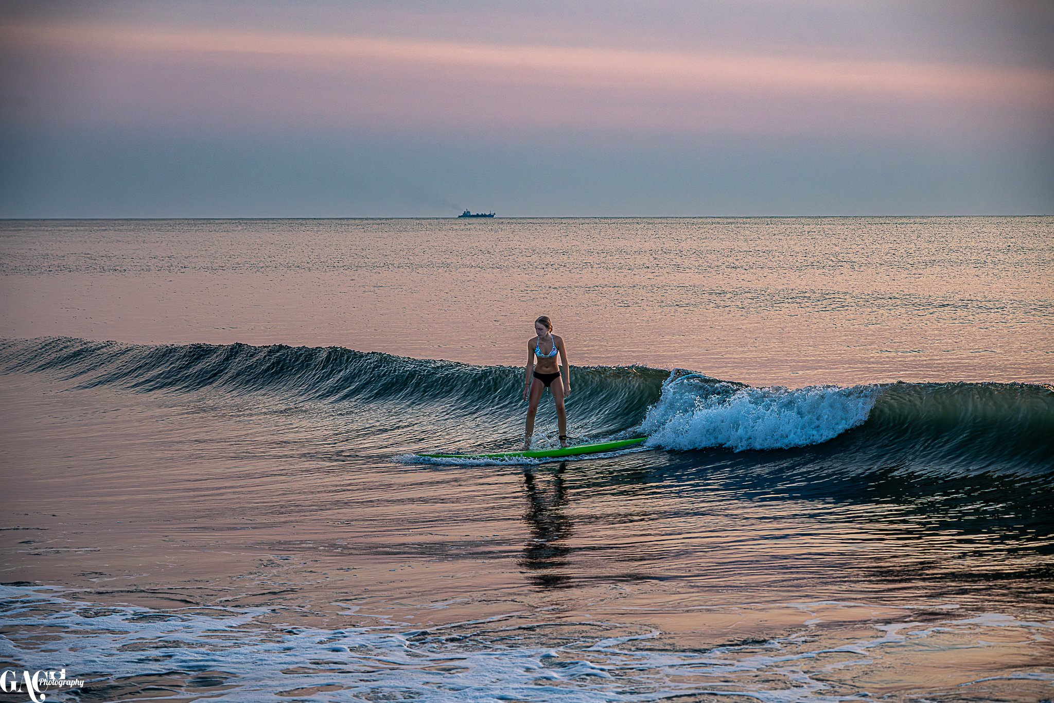 A young woman surfing on a small wave at sunset or sunrise in the ocean.