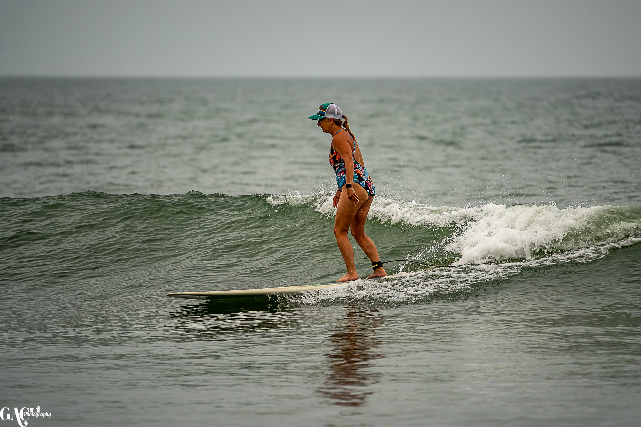 A woman surfing in the ocean on a sunny day, wearing a colorful swimsuit, a cap, and a watch.