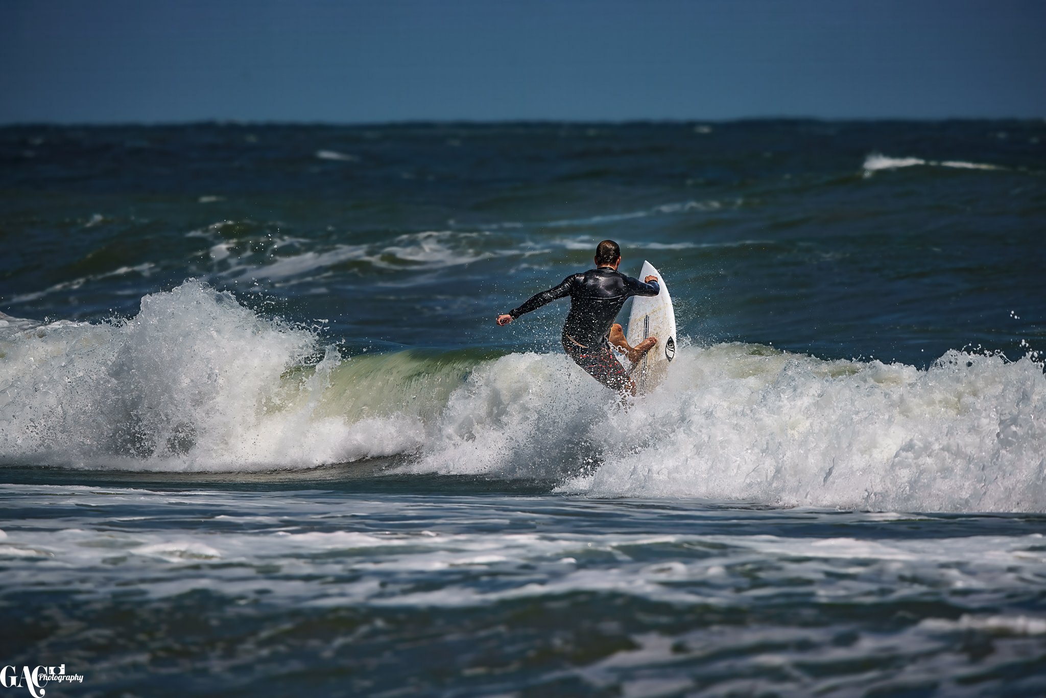 A person in a wetsuit surfing on a white surfboard on a wave at the beach with a dark sky in the background.
