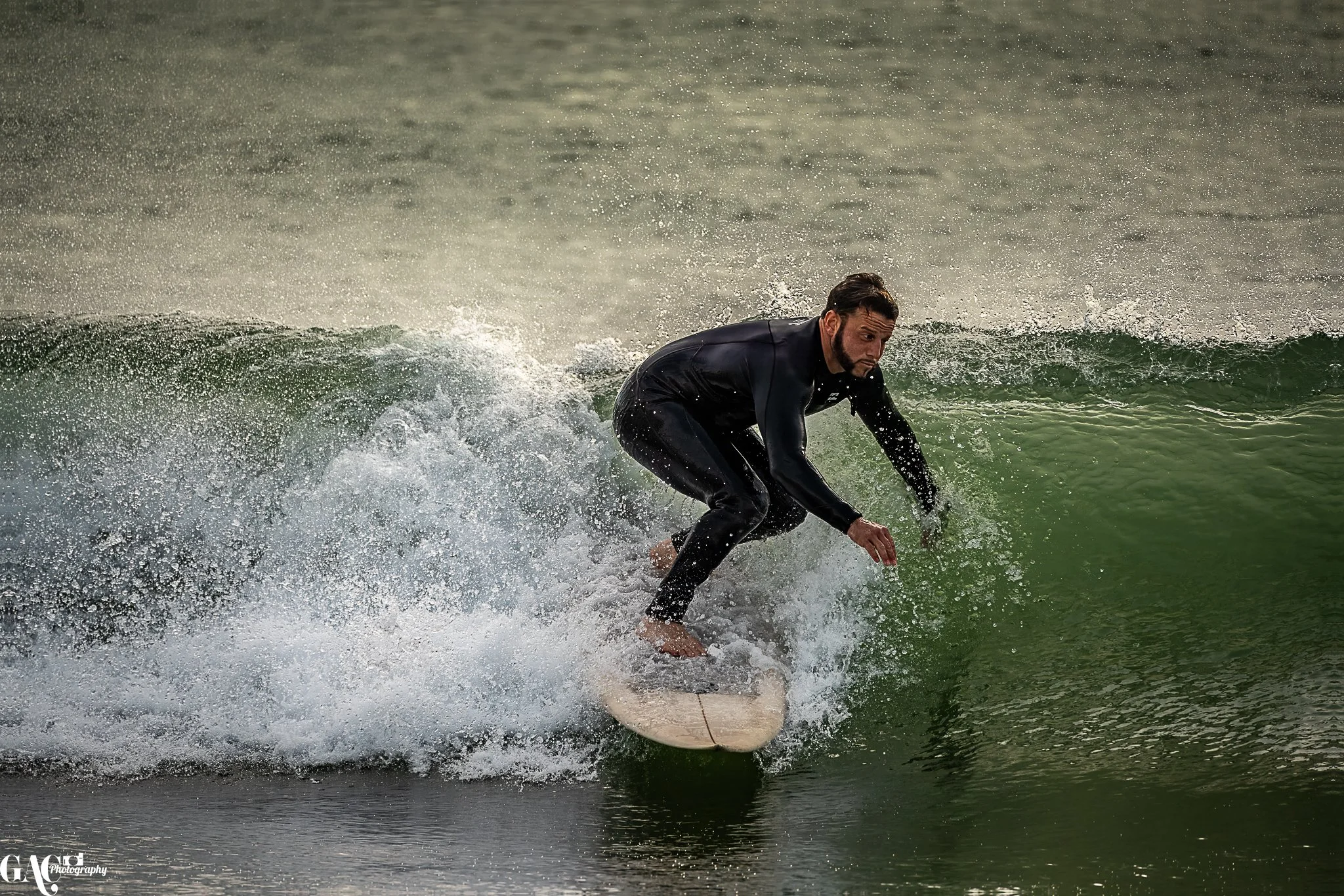 A man in a black wetsuit surfing on a small wave in the ocean.