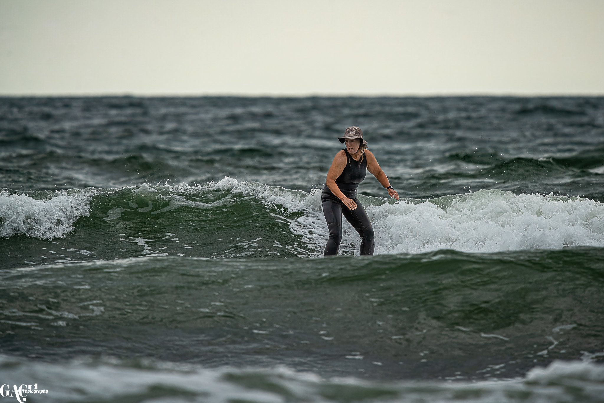 Woman wearing a hat and wetsuit surfing on the ocean waves.