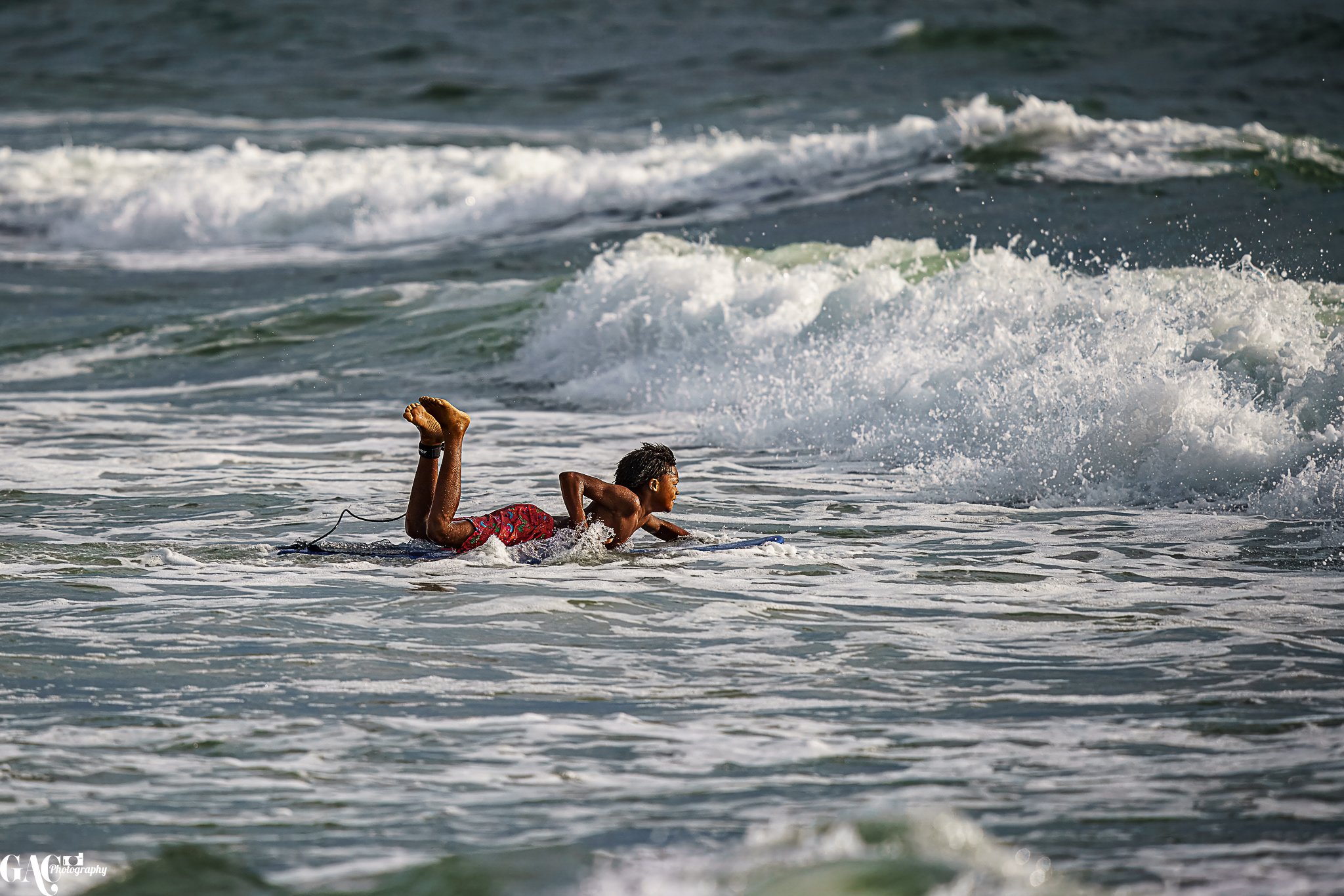 A young boy lying on a surfboard in the ocean, paddling through the waves.