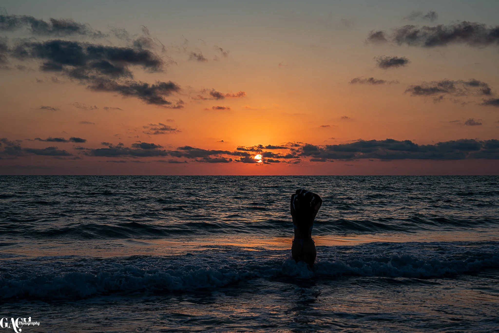 Silhouette of a person in the ocean at sunset with a colorful sky.