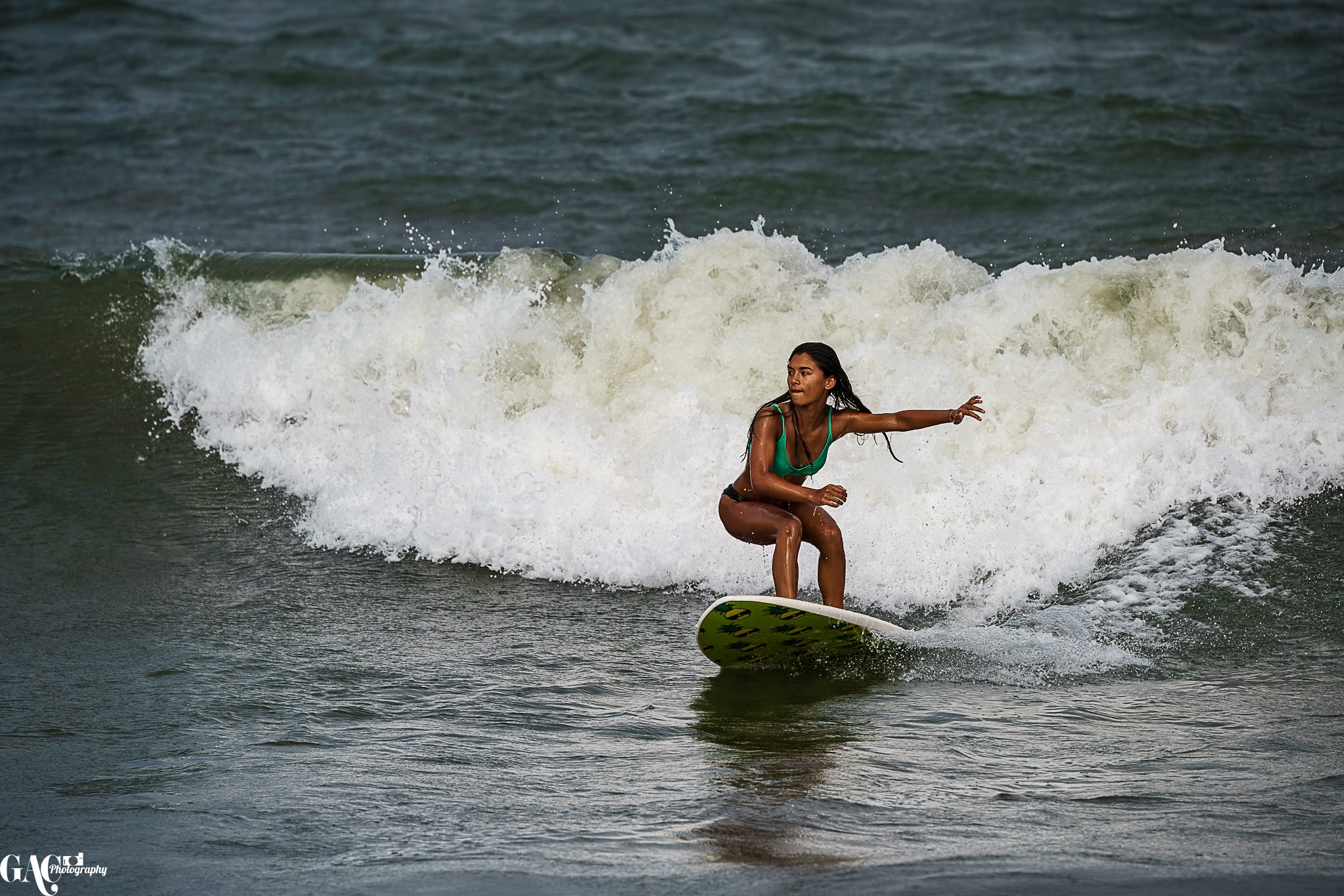 A woman surfing on a green surfboard in the ocean with waves crashing around her