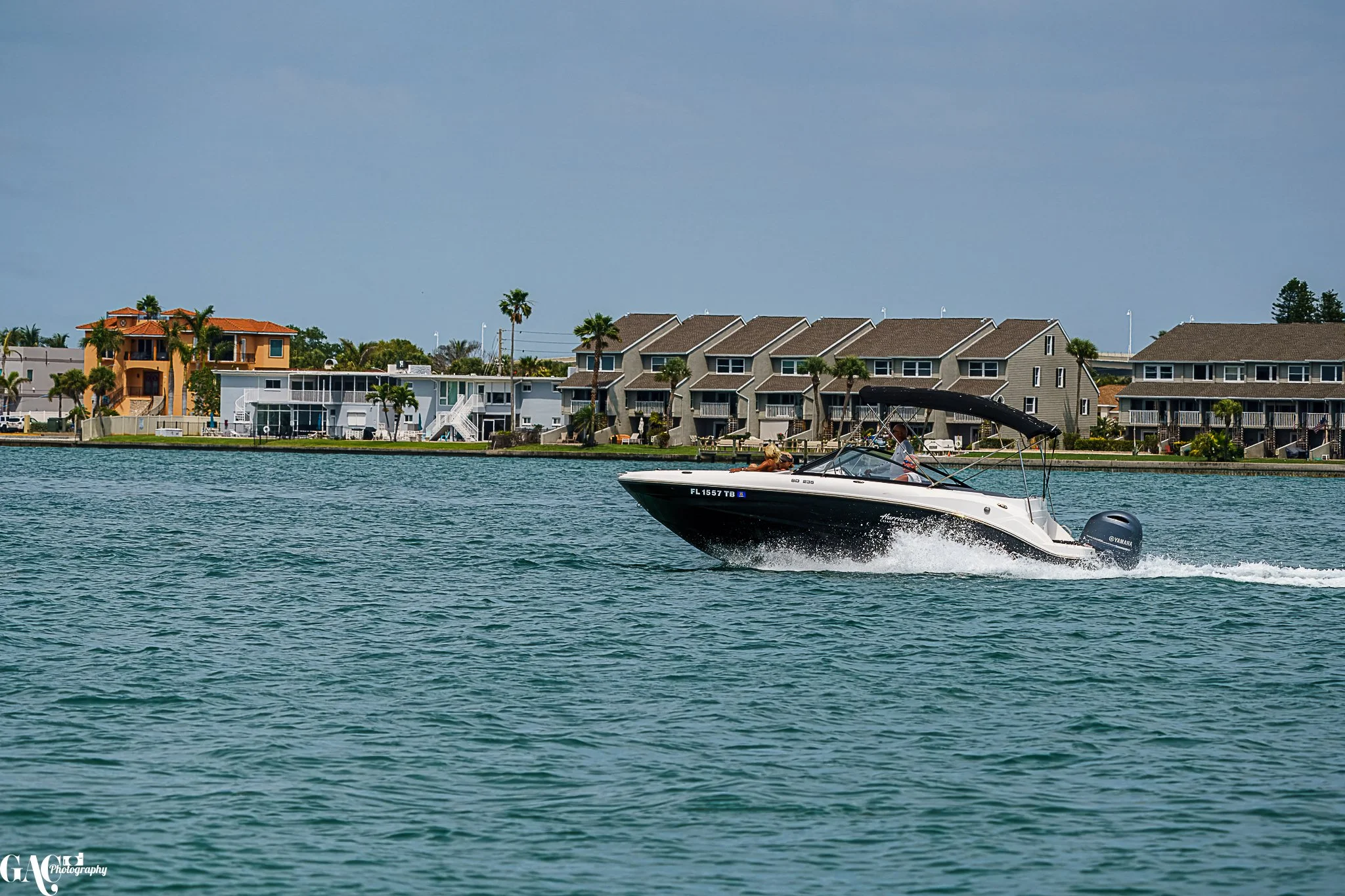A speedboat on water with houses and palm trees in the background on a sunny day.