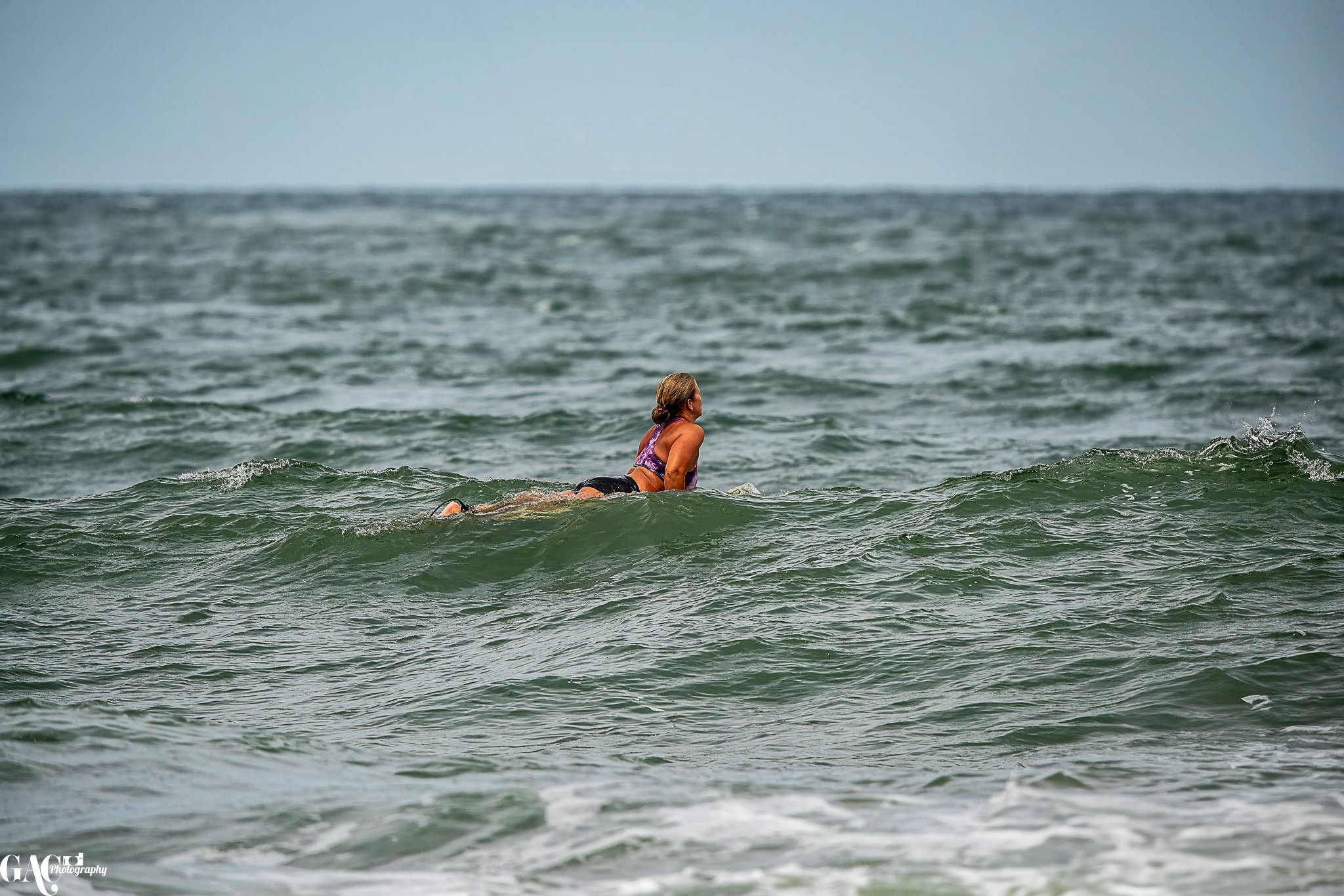 A woman in a purple top and black shorts swimming in the ocean on a cloudy day.