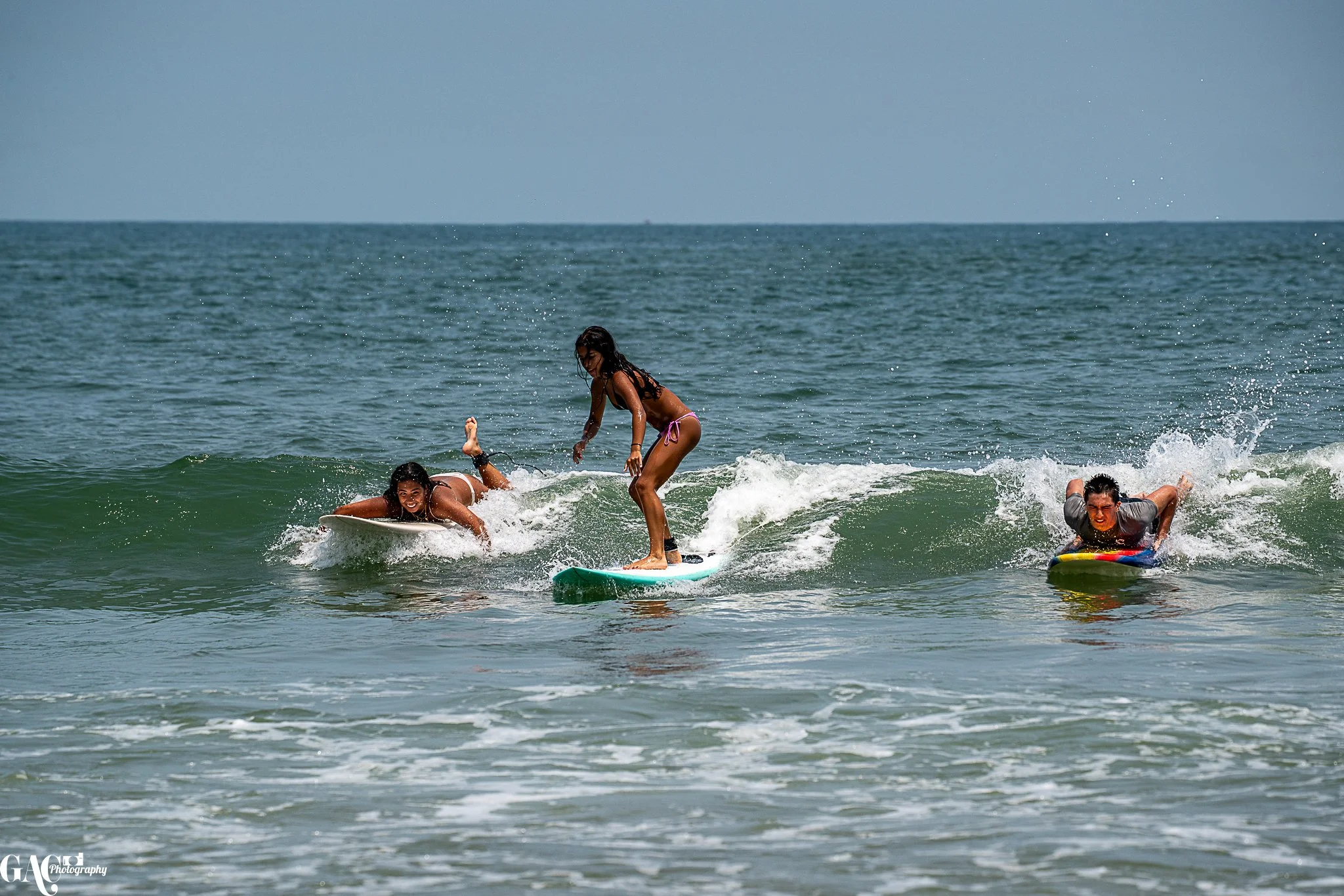 Three girls surfing and playing in the ocean waves on a sunny day.