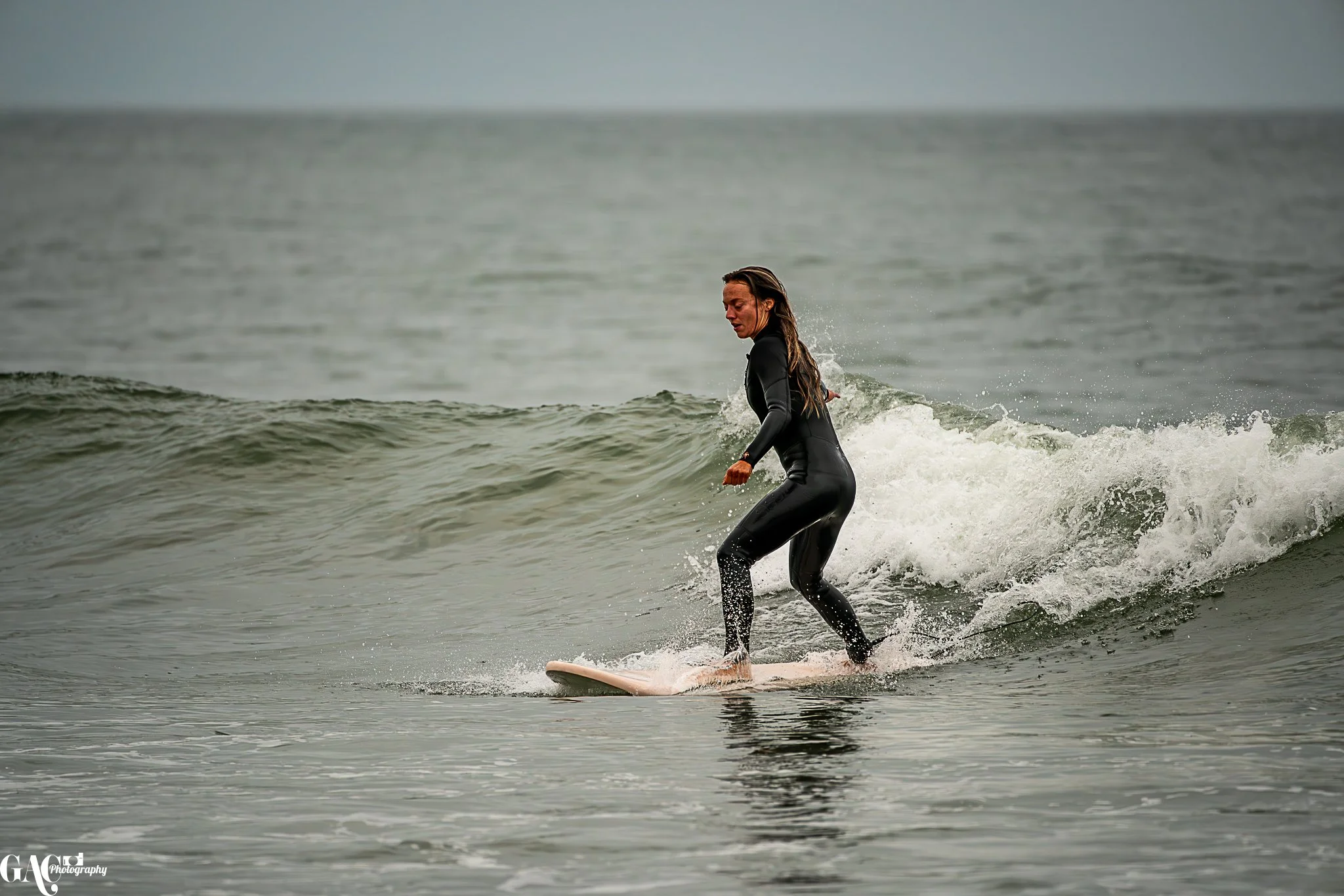 Person surfing on a wave in the ocean, wearing a black wetsuit.