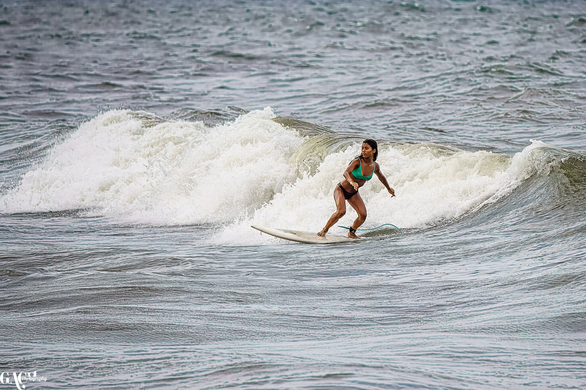 A woman in a green swimsuit surfing on the ocean waves.