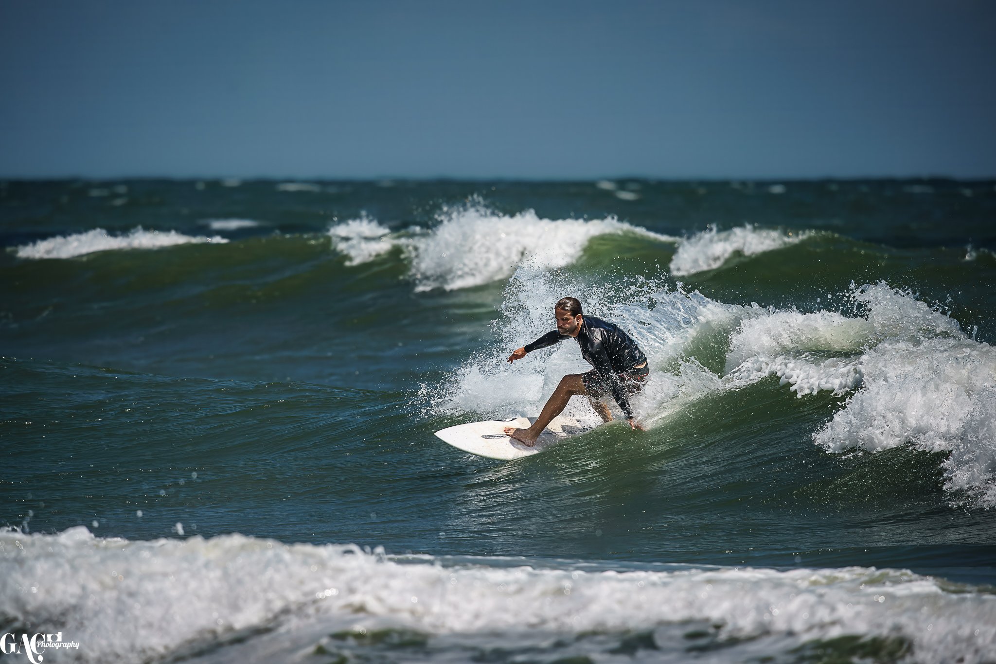 A man surfing on a wave in the ocean, wearing a black wetsuit and riding a white surfboard.