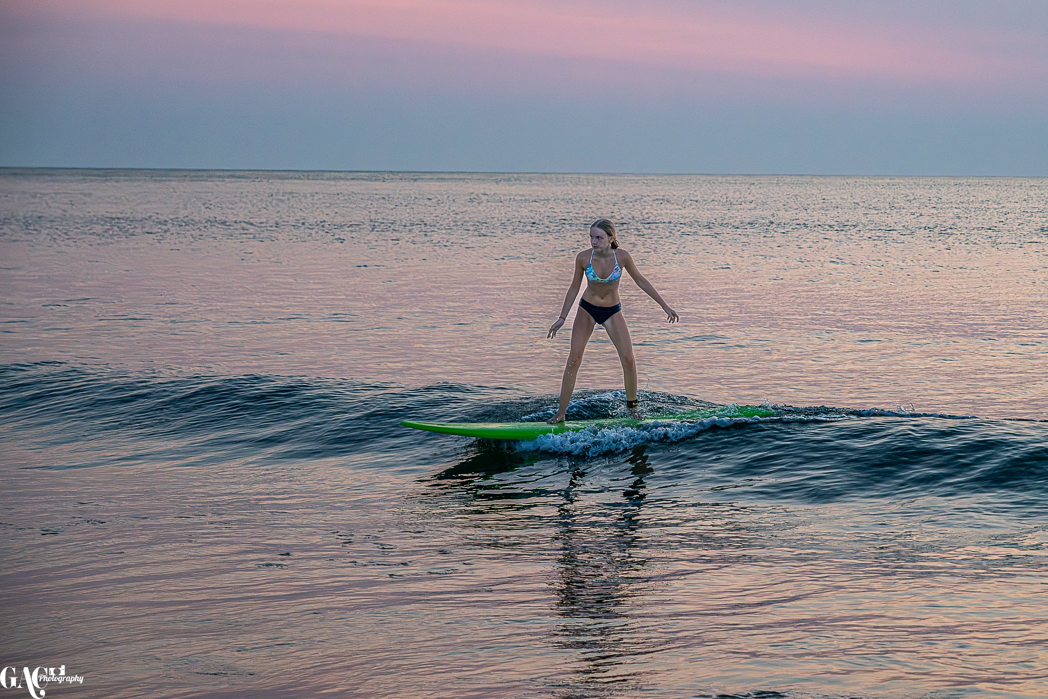 A girl surfing on a green surfboard in the ocean during sunset or sunrise.