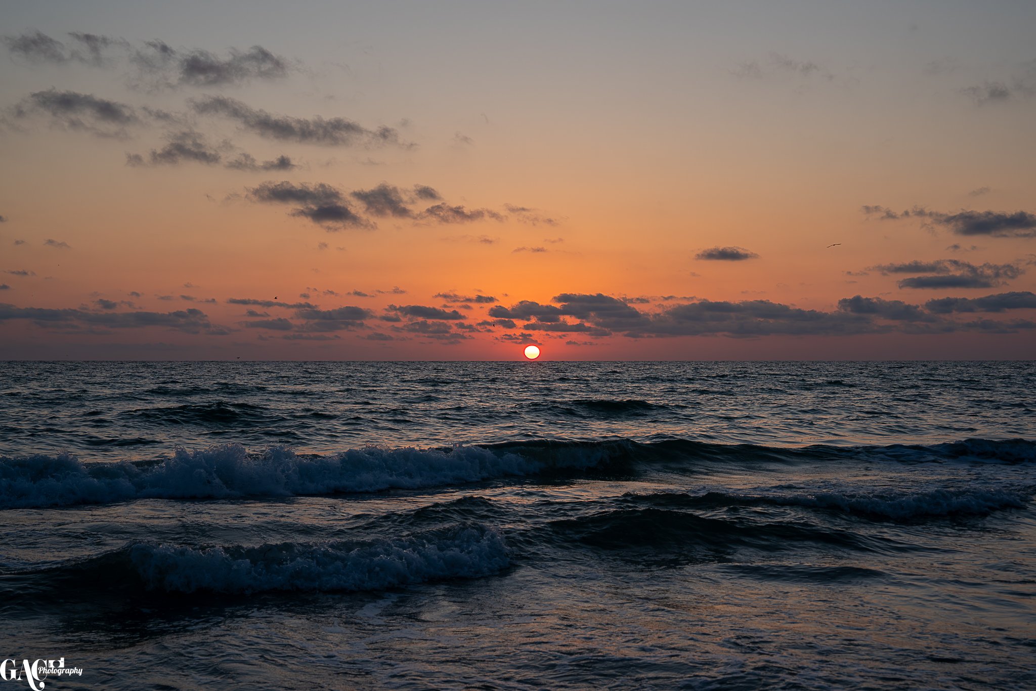 Sunset over the ocean with waves and clouds in the sky.