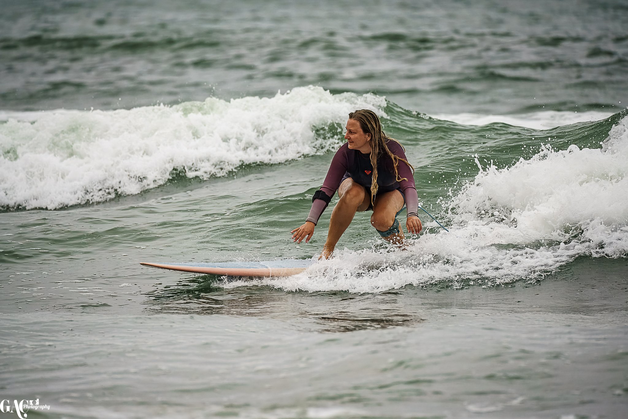 A woman surfing on a wave in the ocean, wearing a wetsuit.