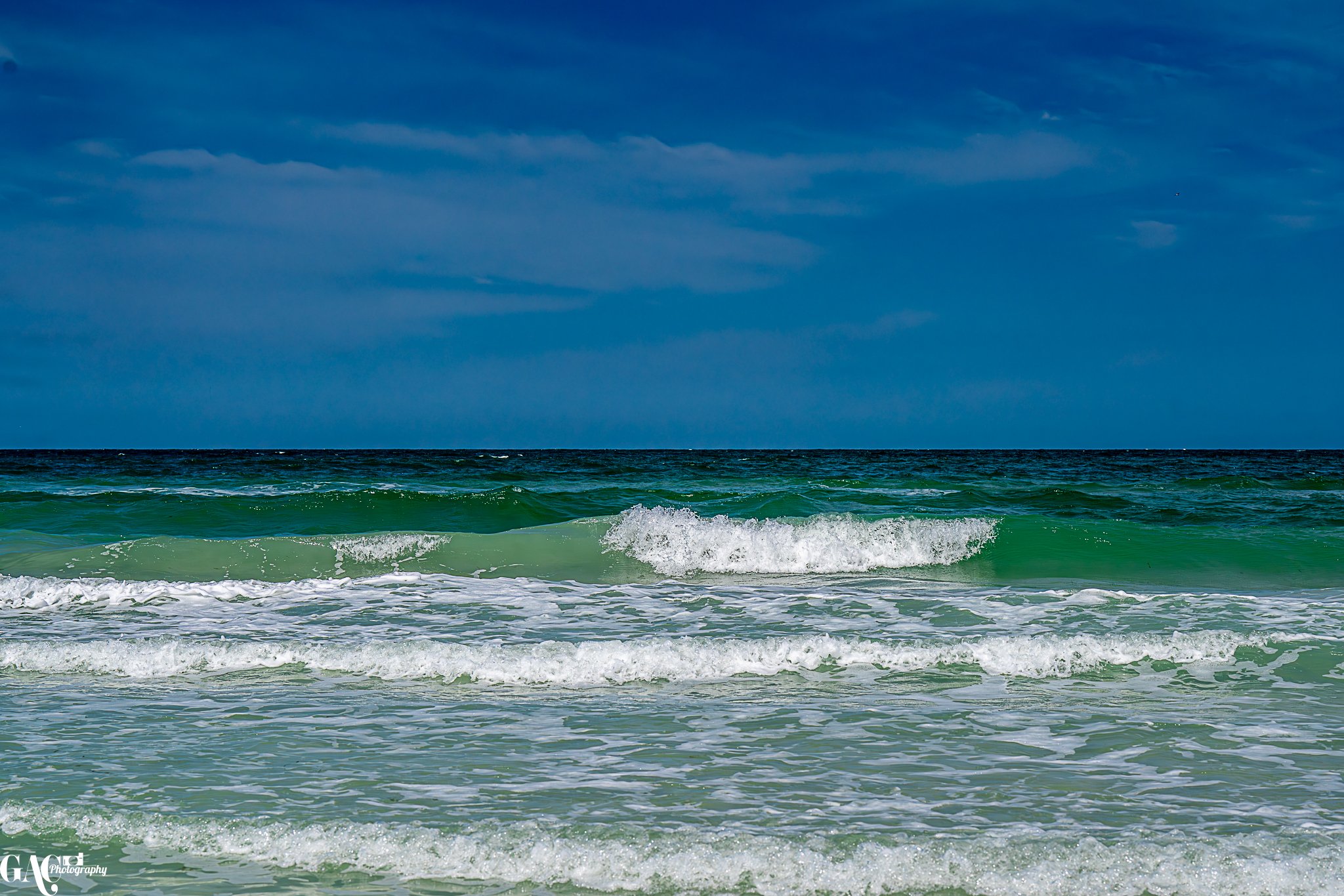 Ocean waves crashing on a sandy beach with a blue sky and some clouds.