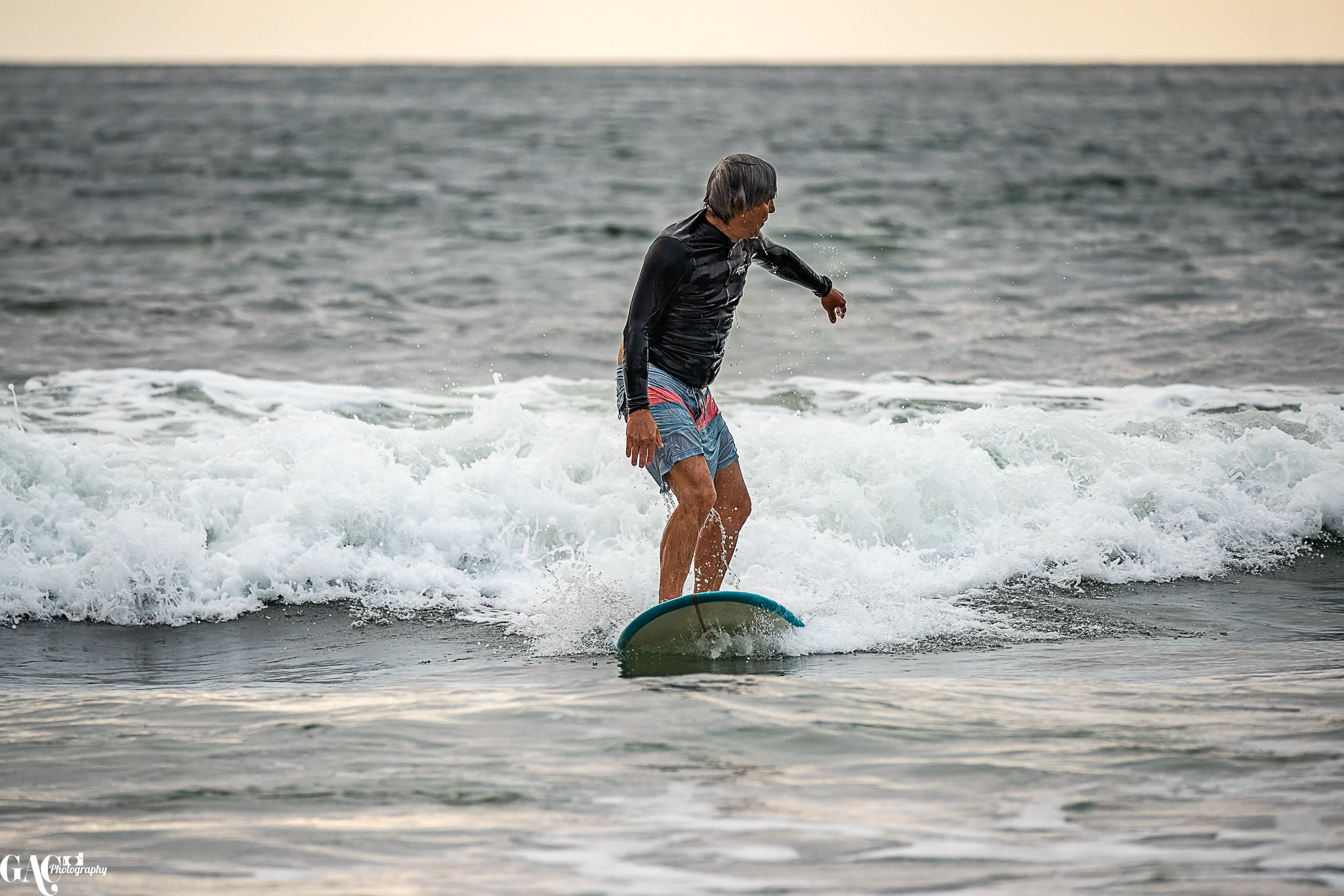 An older man surfing on a surfboard in the ocean during daytime.