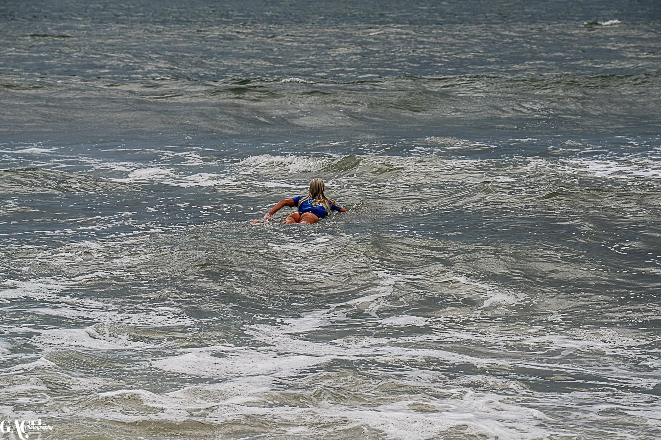 Child wearing a blue swimsuit swimming in the ocean with waves.