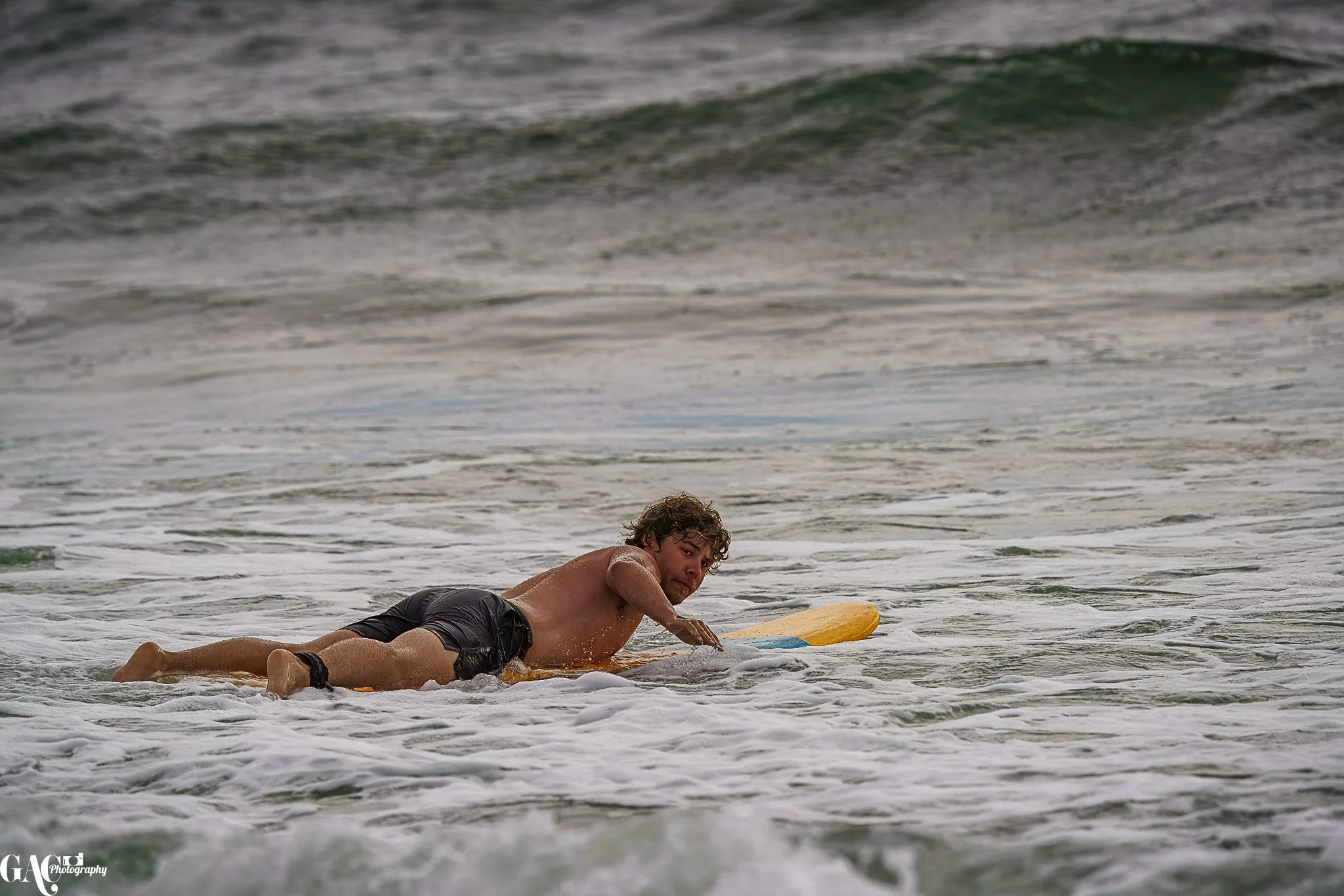 A man lying on a yellow surfboard in the ocean, preparing to surf.